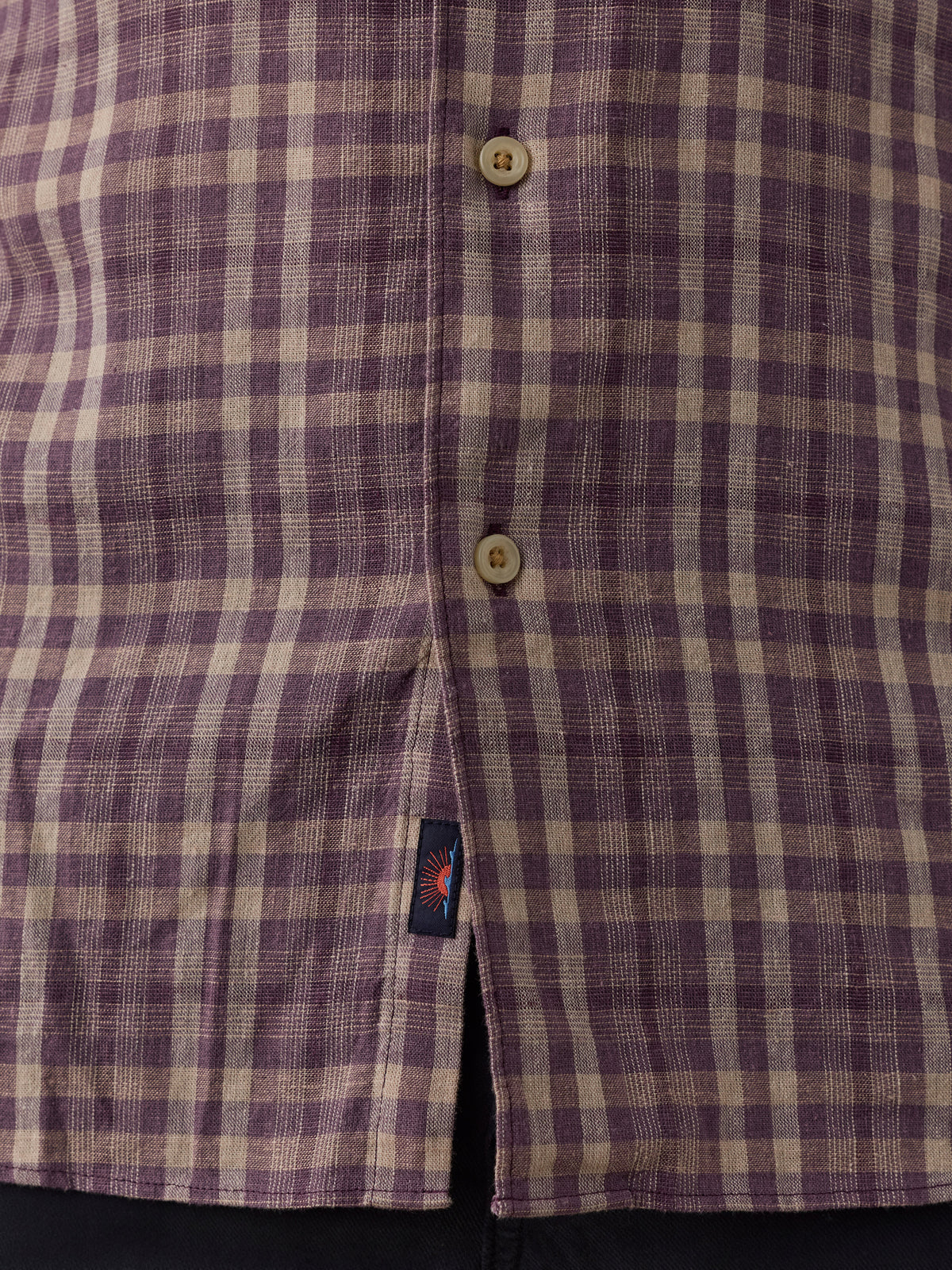 Close-up of a purple and beige plaid button-down shirt fabric, showing the button placket and a small Faherty brand tag near the hem., image 4 of 6
