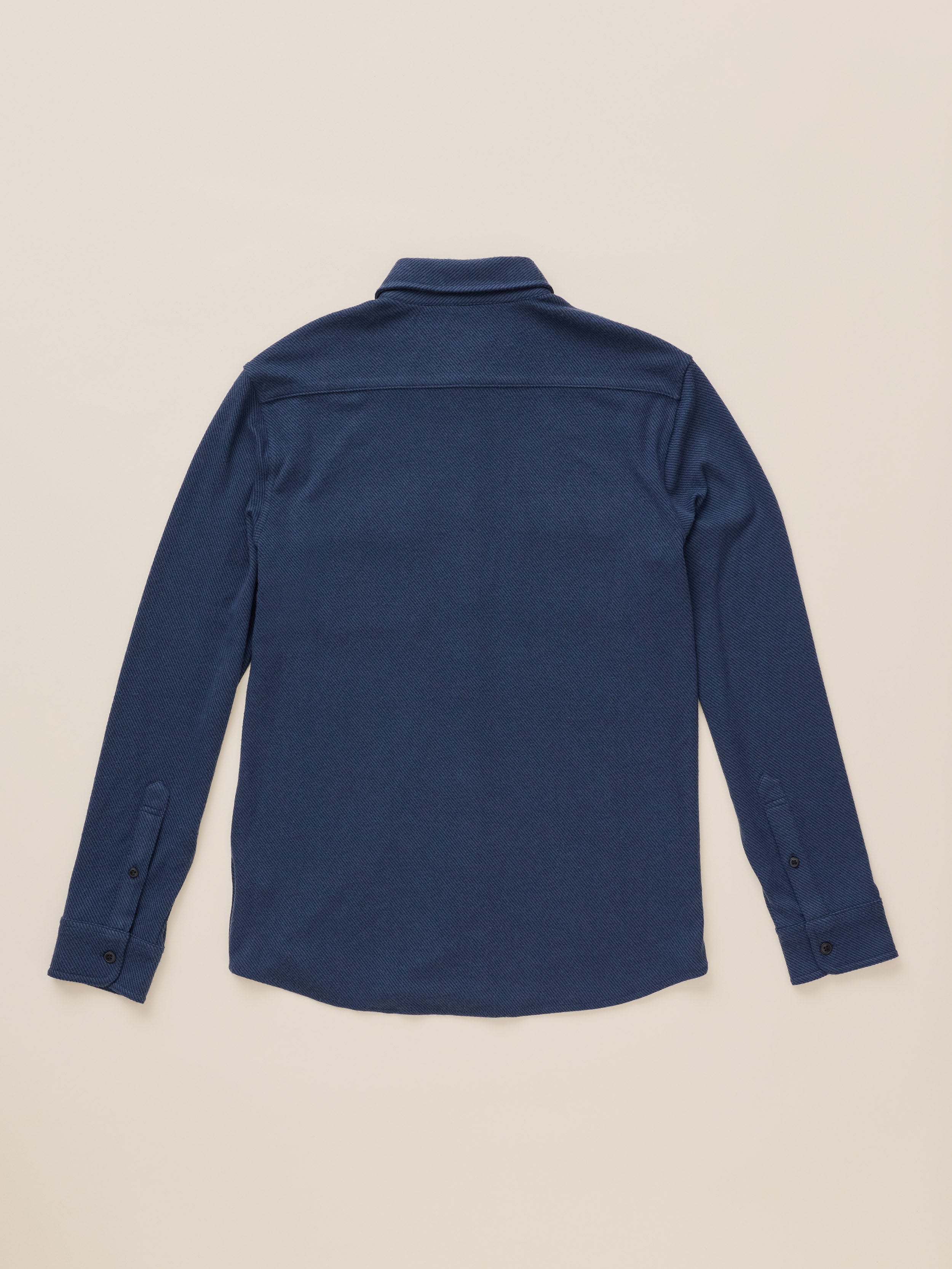 A dark blue long-sleeve button-up shirt shown from the back, laid flat against a light beige background.