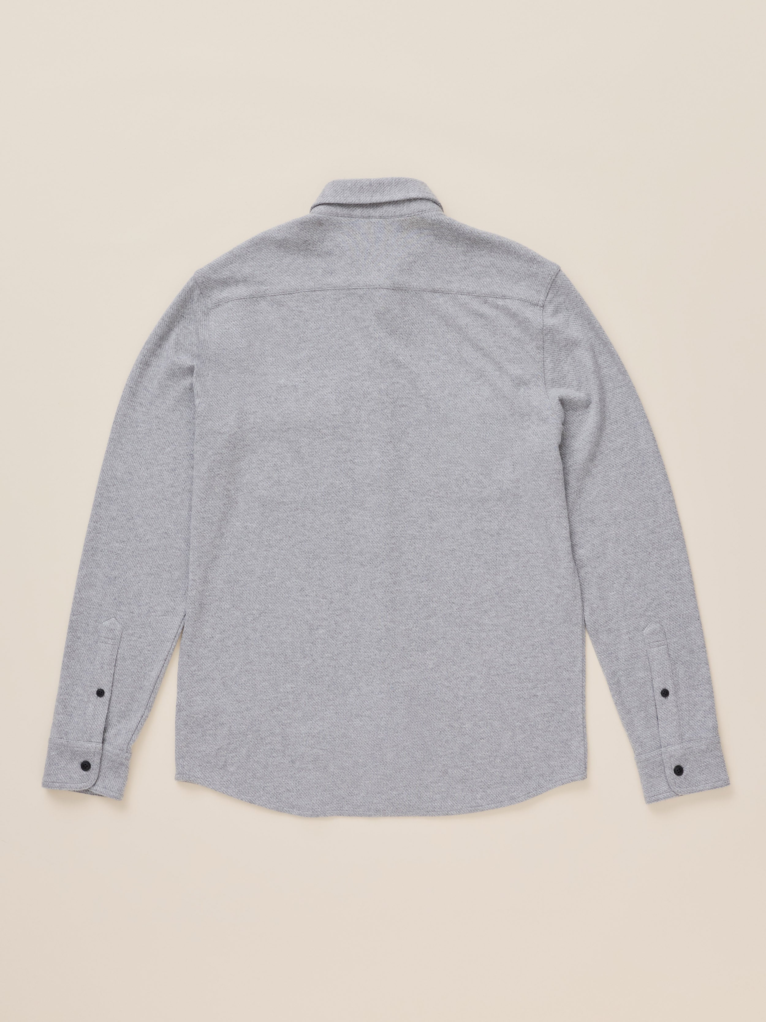 A light gray heather long-sleeve button-up shirt shown from the back, laid flat on a warm beige background.