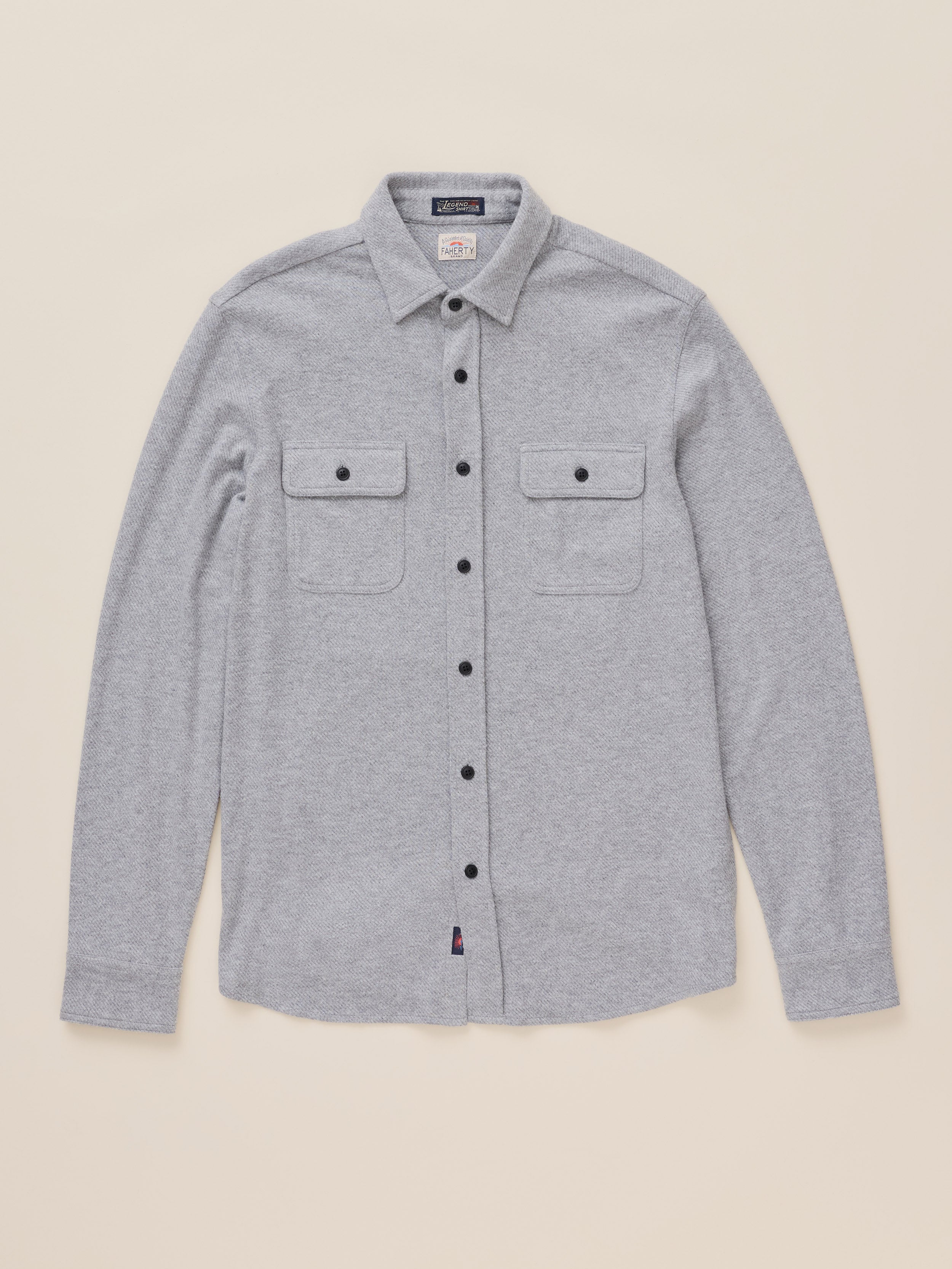 A light gray heather long-sleeve button-up shirt with two buttoned chest flap pockets, laid flat against a solid beige background.
