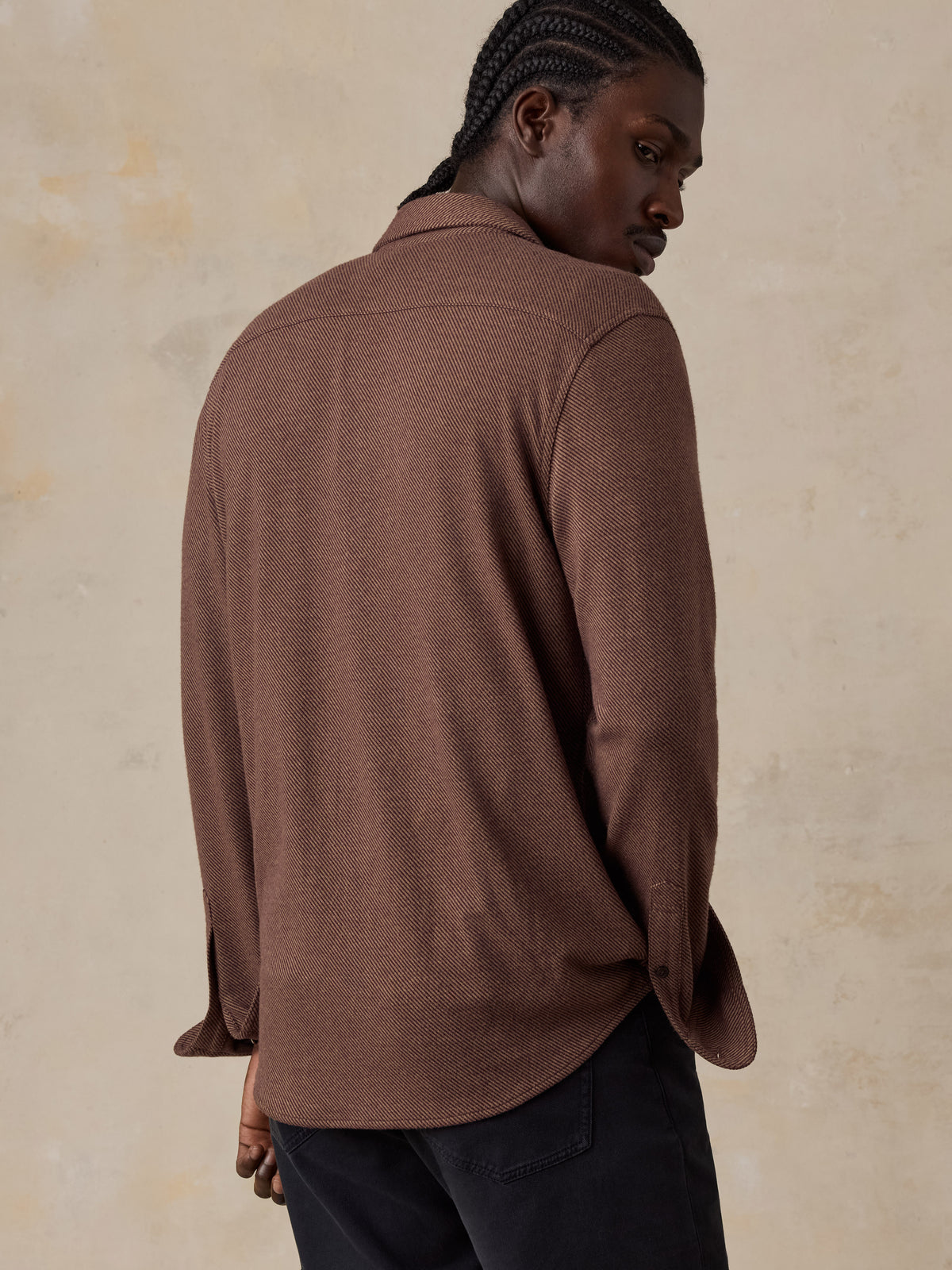 A man viewed from behind wearing a brown shirt and black jeans, image 3 of 5
