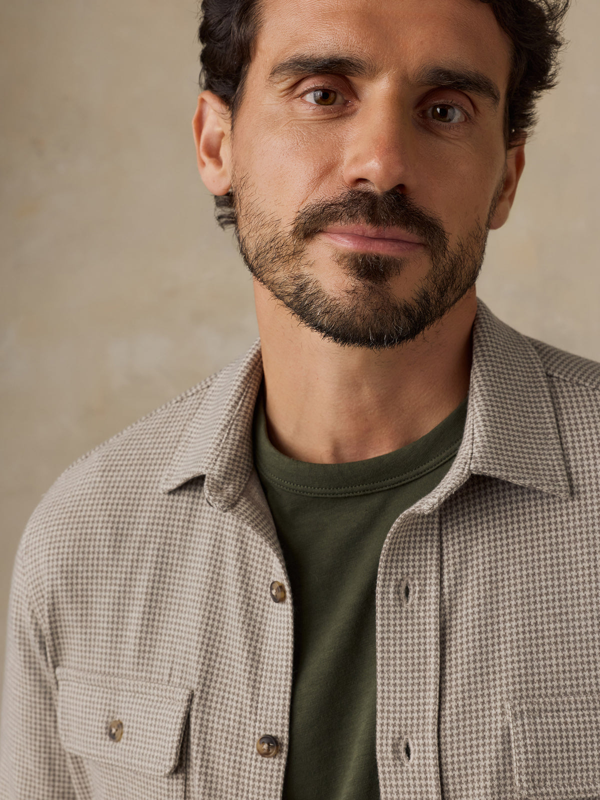 Man wearing a beige overshirt with a green t-shirt against a beige studio background, image 4 of 7