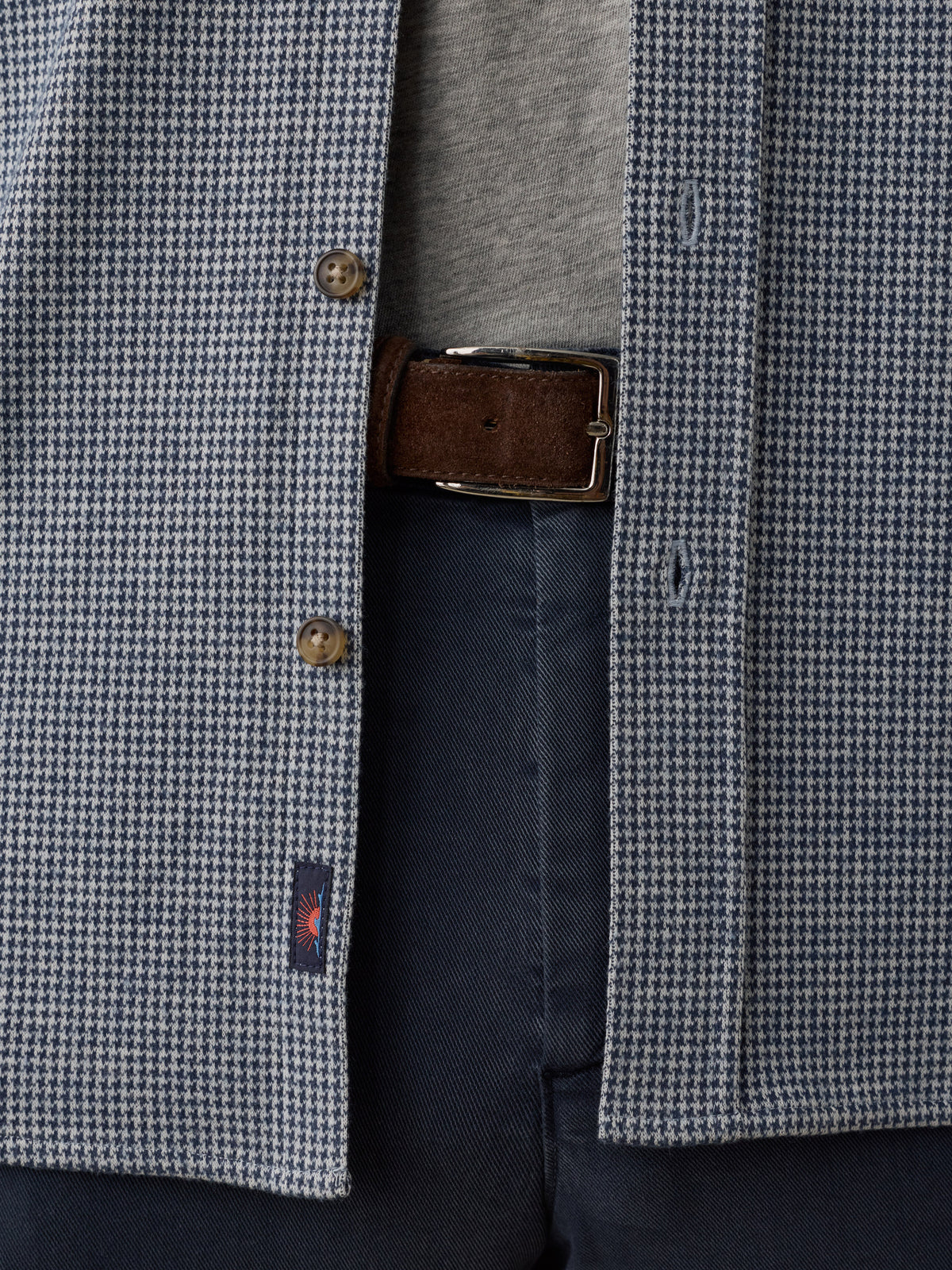 Close-up of a houndstooth patterned blazer in blue and white, worn open over a gray shirt and navy trousers, with a brown belt and metal buckle visible., image 6 of 7