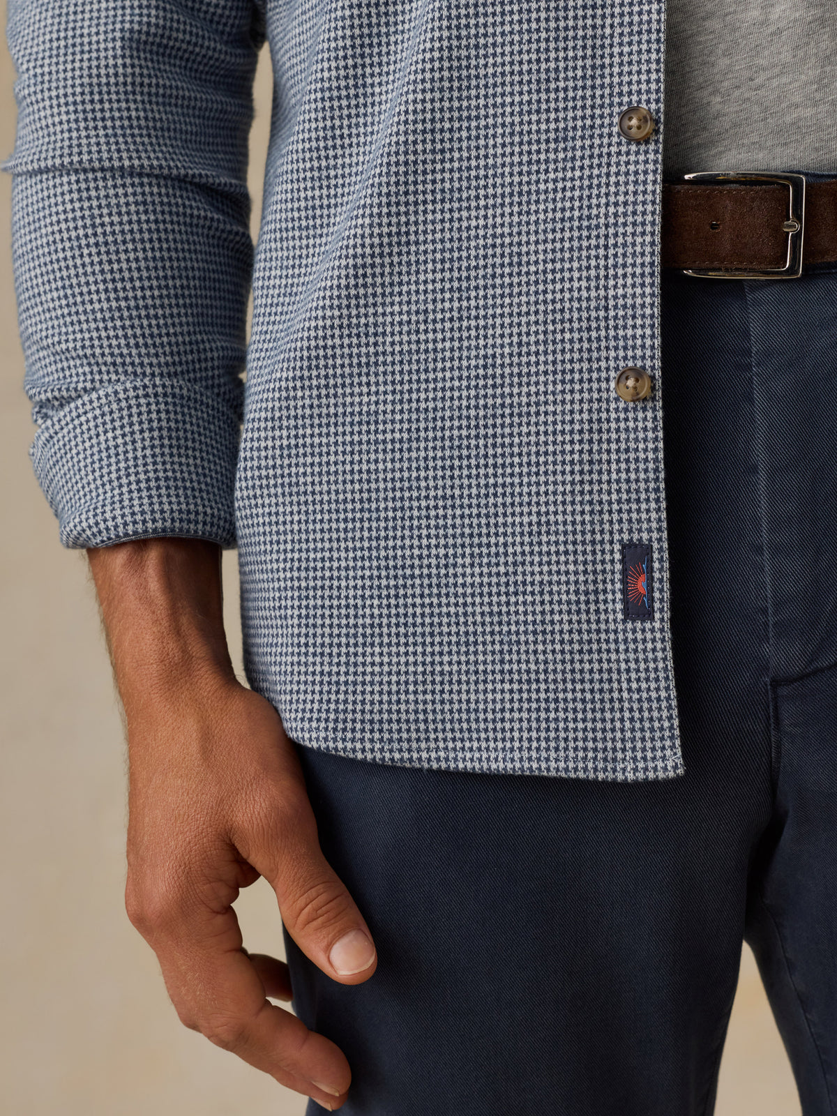 Close-up of a man wearing a blue and white houndstooth patterned button-up shirt, navy trousers, and a brown leather belt., image 5 of 7