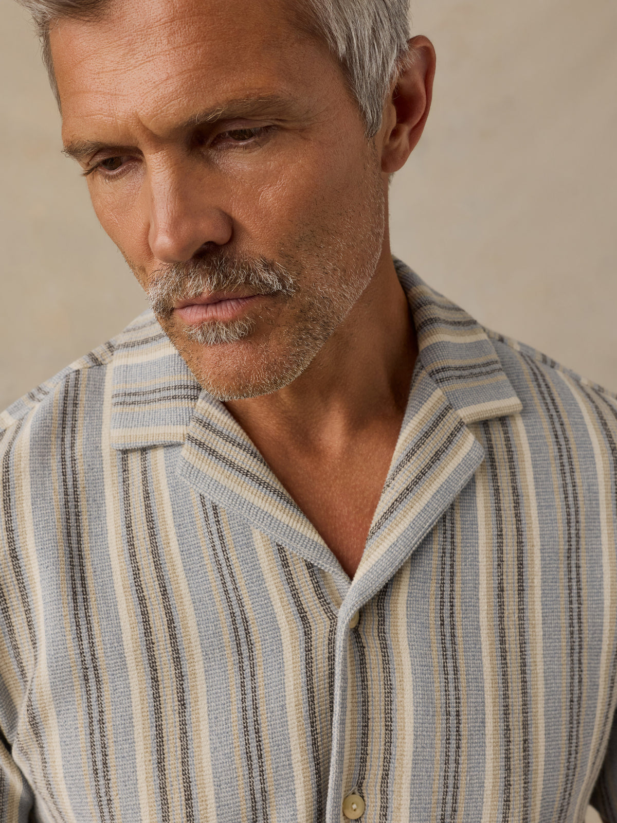 A close-up of a man wearing a textured, vertically striped button-down shirt in beige, light blue, and dark gray., image 2 of 6