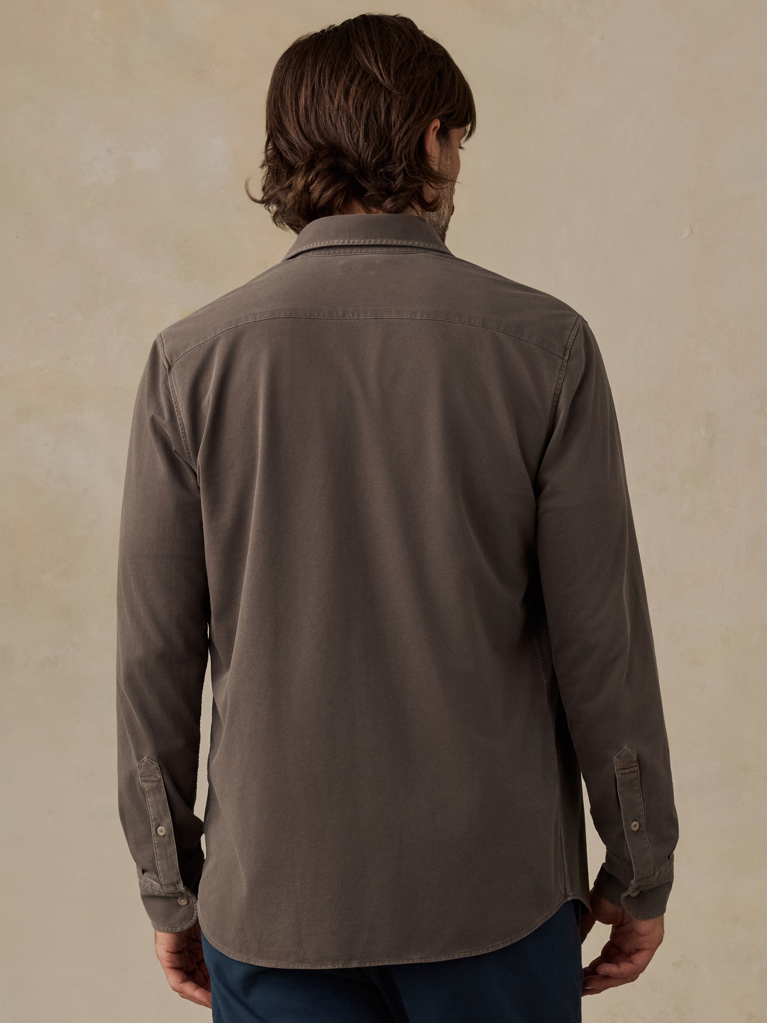 Man wearing a brown button down shirt and navy chino pants against a beige background