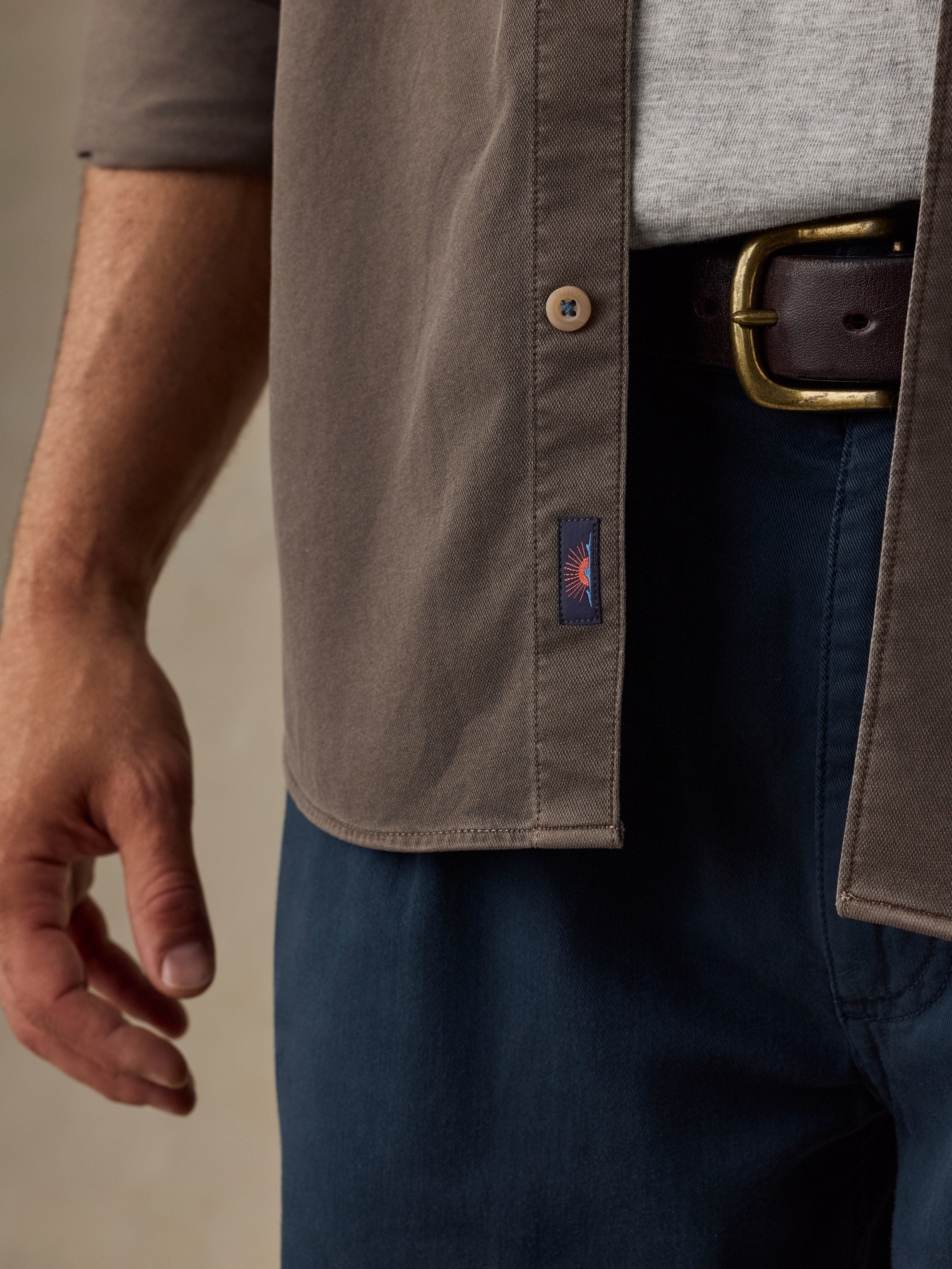 Man wearing a brown button down shirt and navy chino pants against a beige background