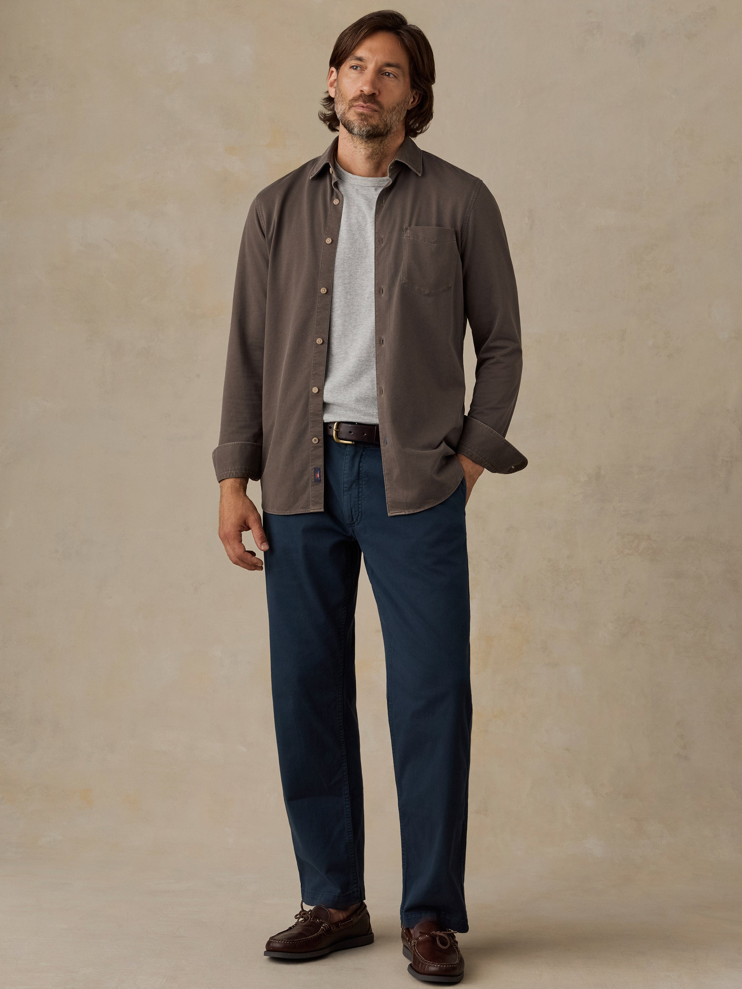 Man wearing a brown button down shirt and navy chino pants against a beige background