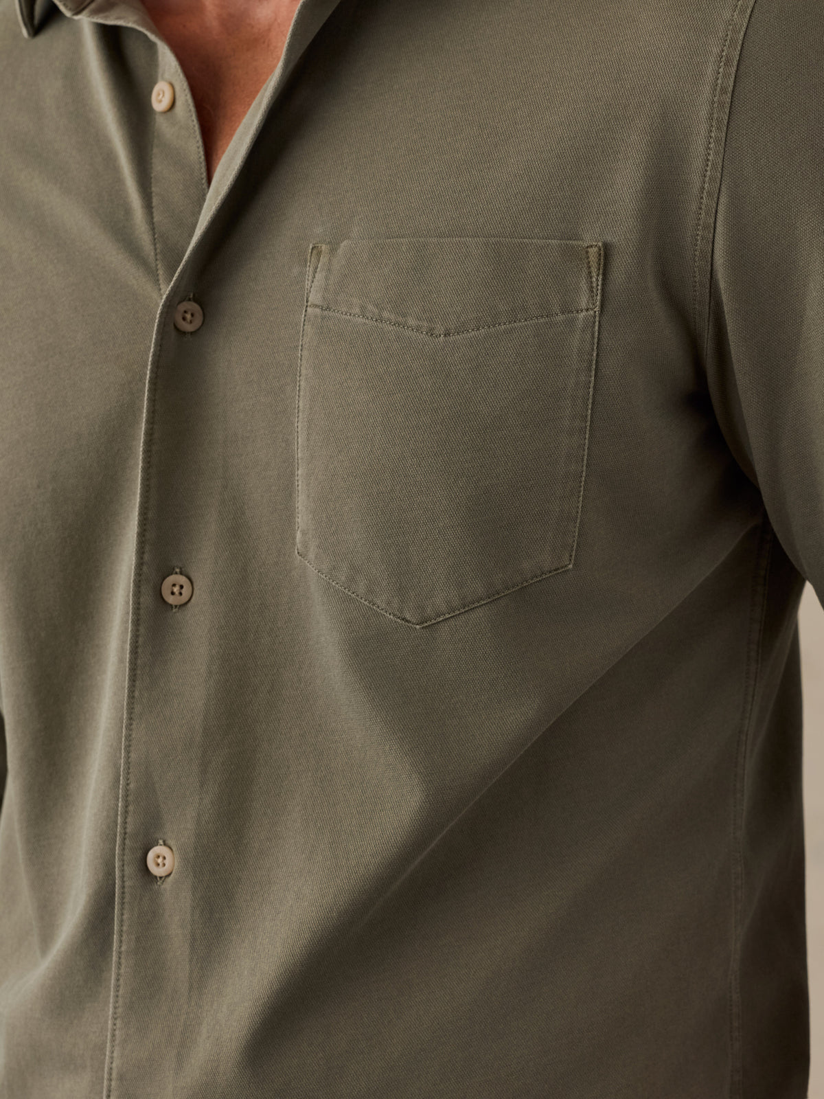 Close-up of a man wearing an olive green long-sleeve button-down shirt with a chest pocket and brown buttons., image 4 of 6