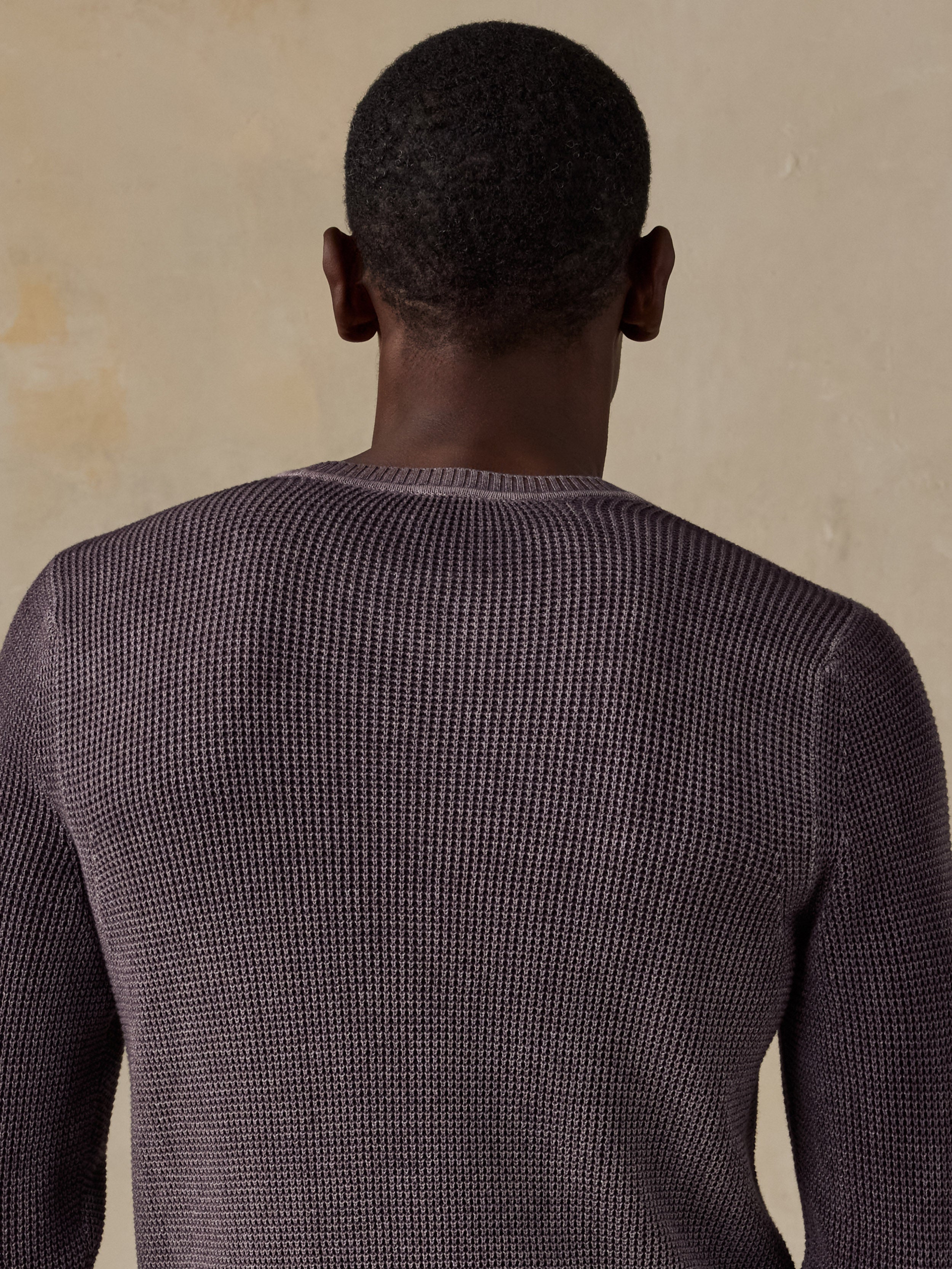 Man wearing a purple knit sweater against a beige background