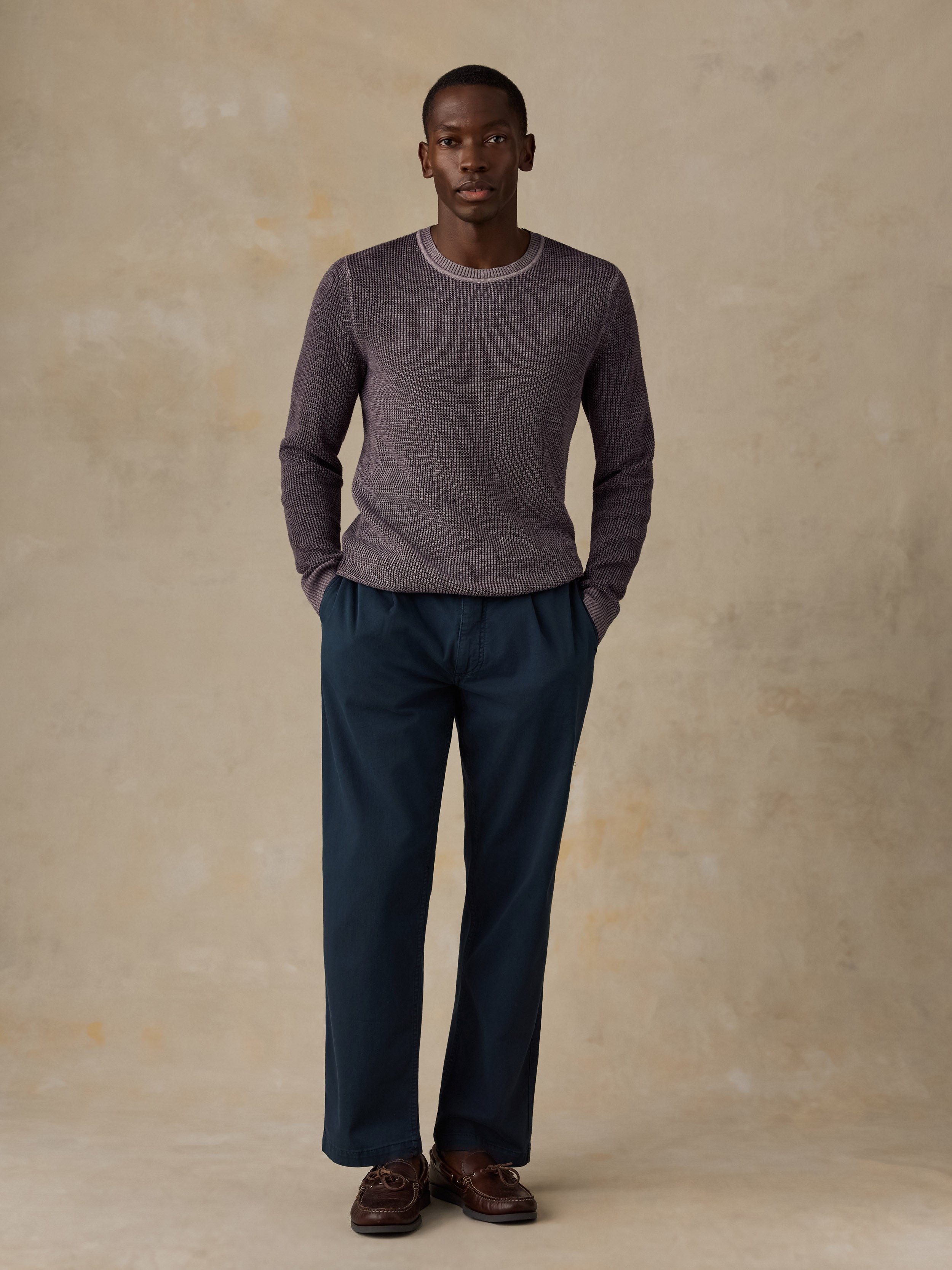 Man wearing a purple knit sweater, navy chino pants, and boat shoes against a beige background