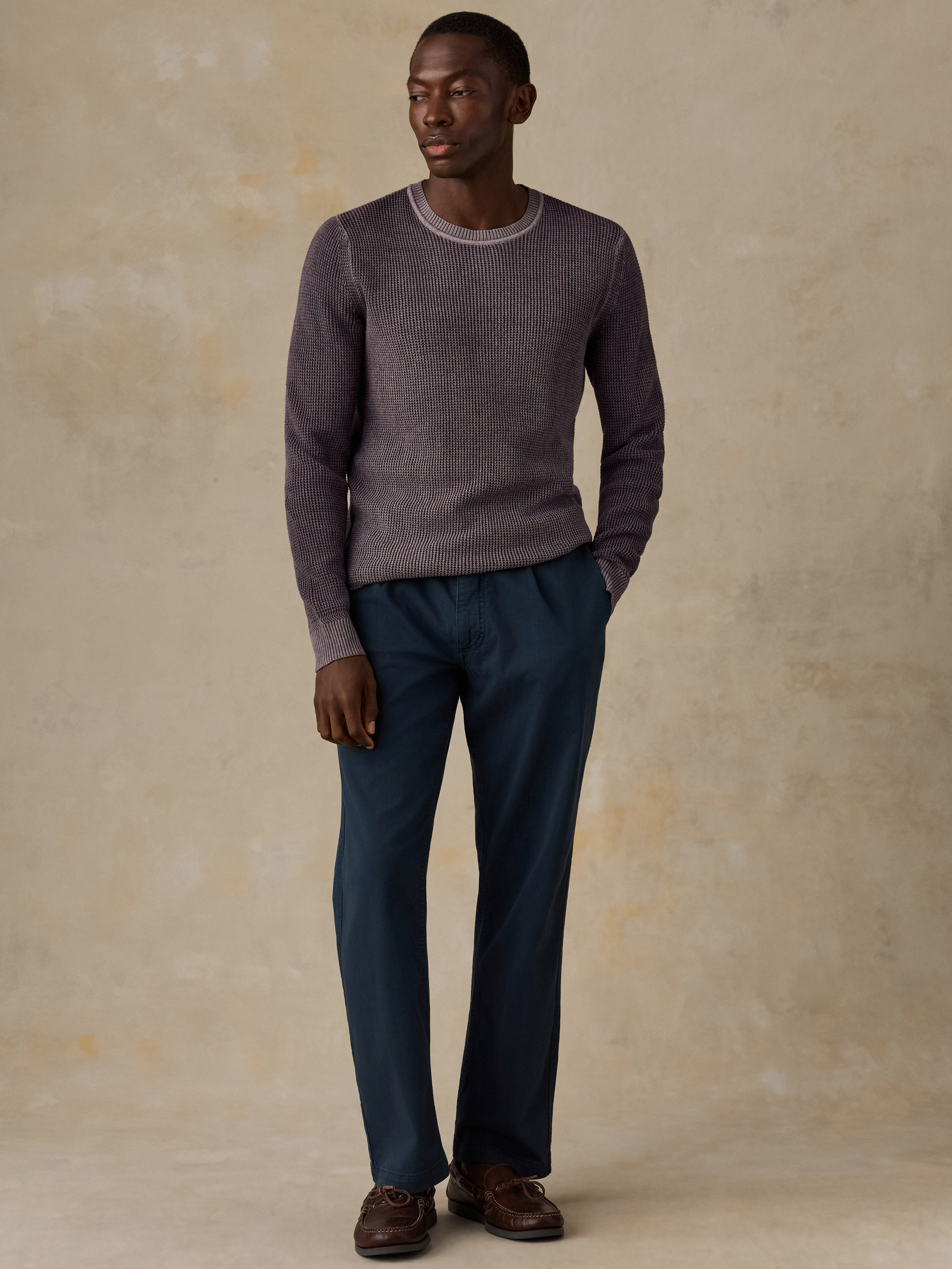 Man wearing a purple knit sweater, navy chino pants, and boat shoes against a beige background
