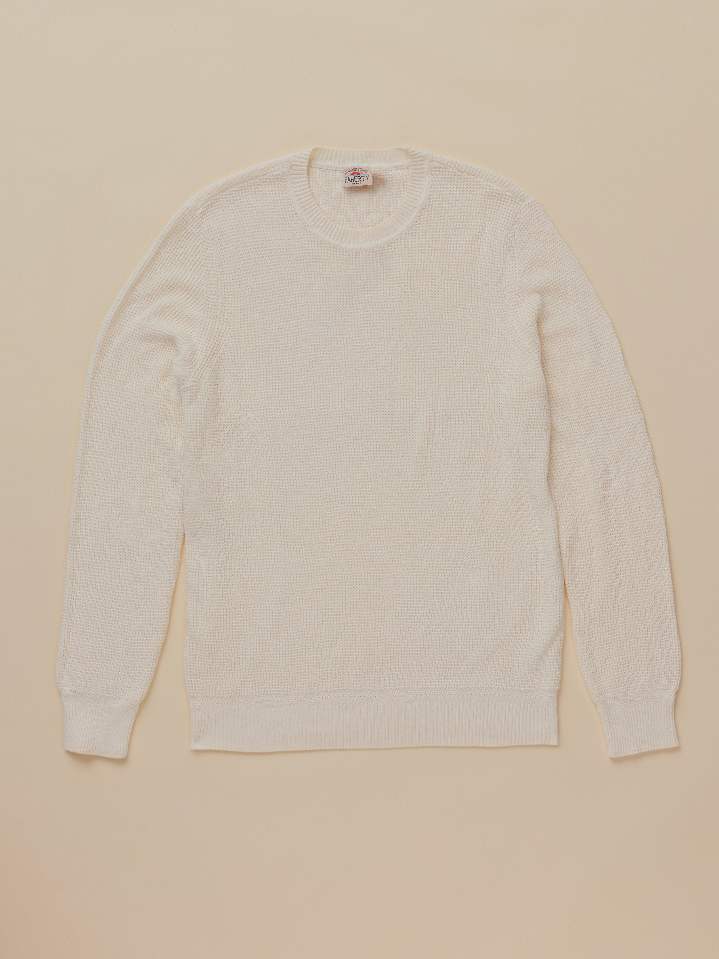 A cream-colored long-sleeve crewneck sweater laid flat against a solid beige background.