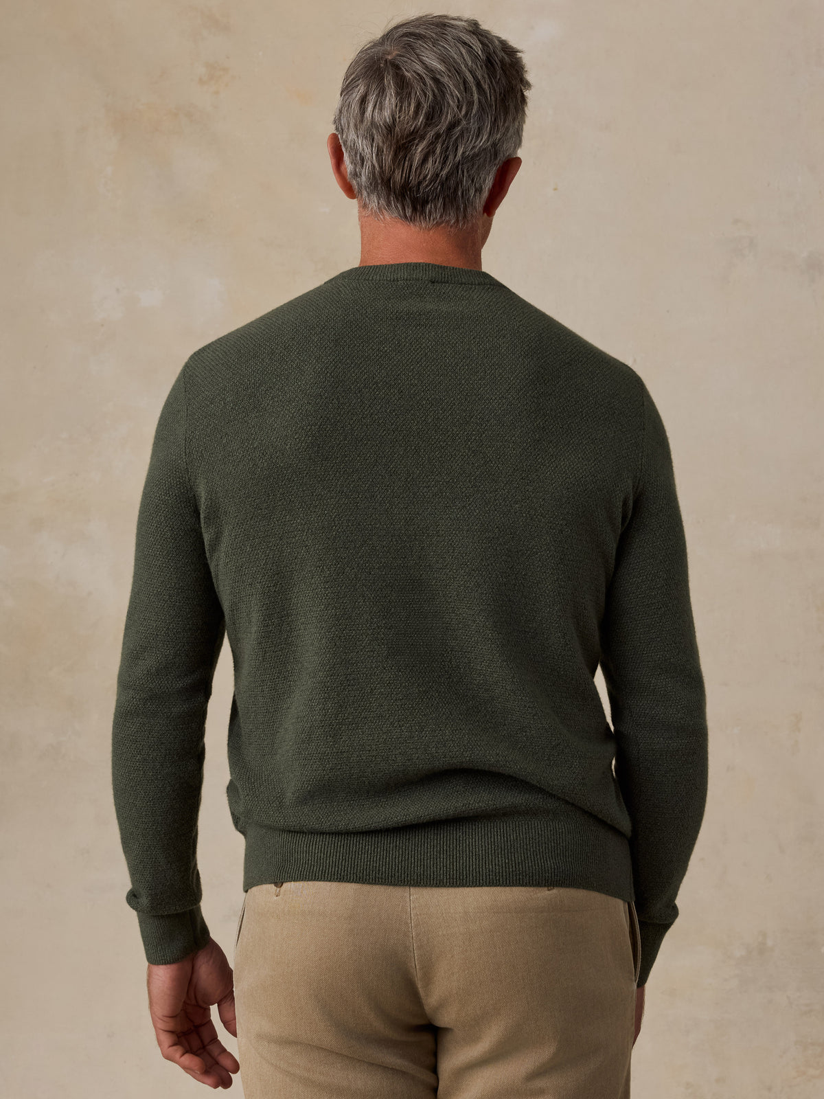 A man viewed from the back wearing a dark green sweater and beige pants, image 3 of 5