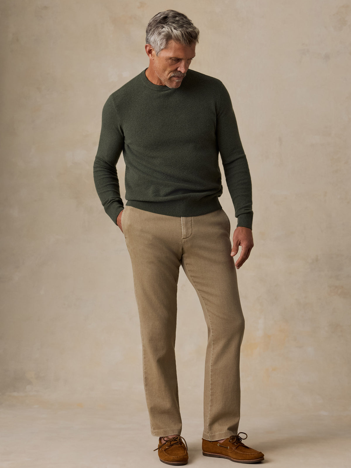 A man wearing a dark green sweater and beige pants, image 5 of 5