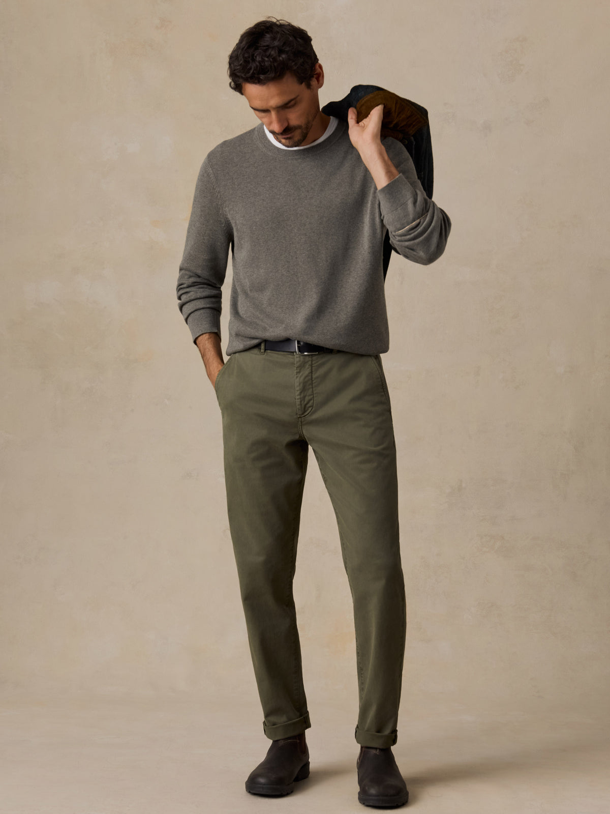 A man wearing a green long-sleeve knit sweater, olive green trousers, and dark brown shoes.