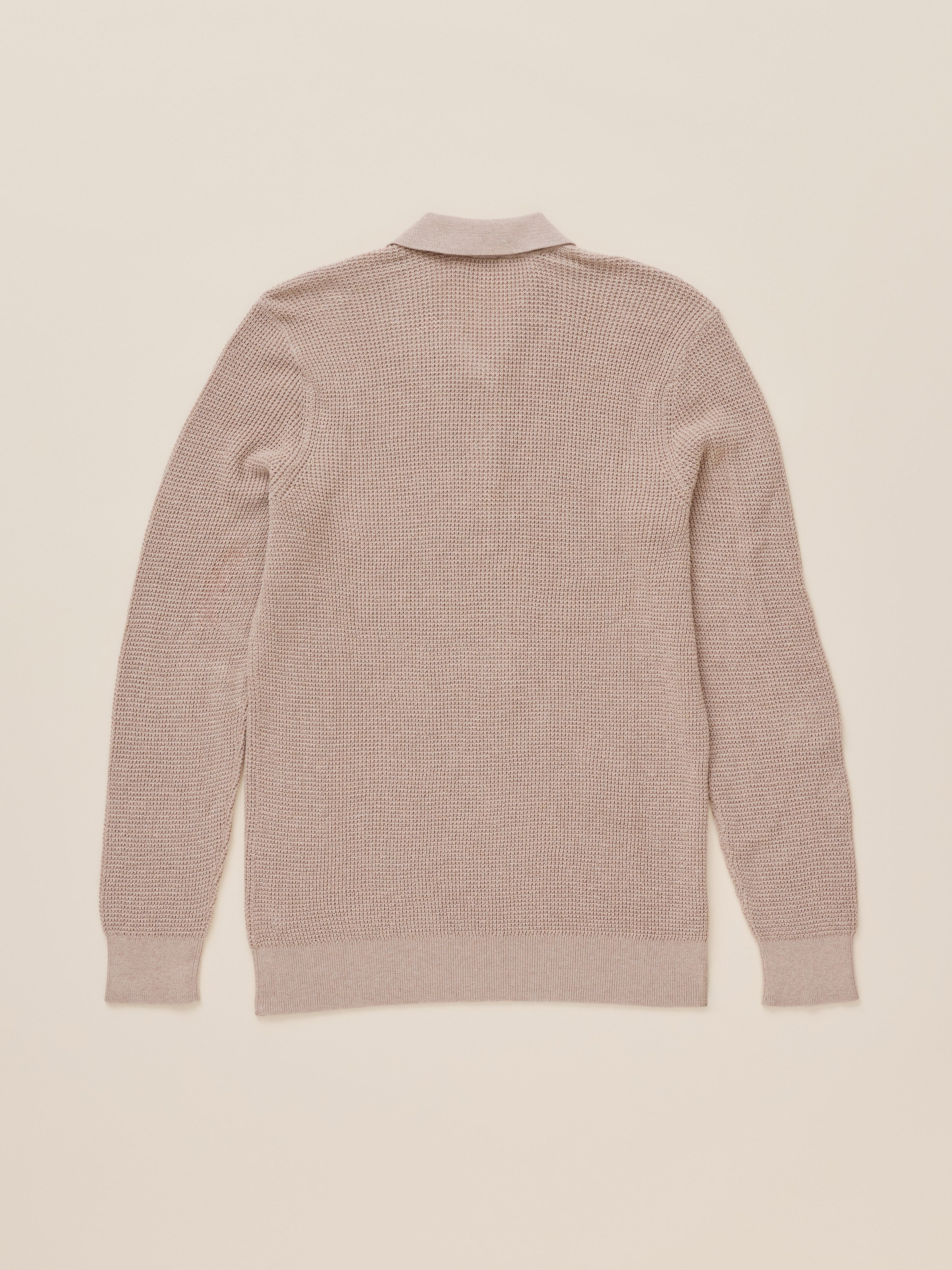 A light beige knit polo shirt shown from the back, laid flat against a matching light beige background.