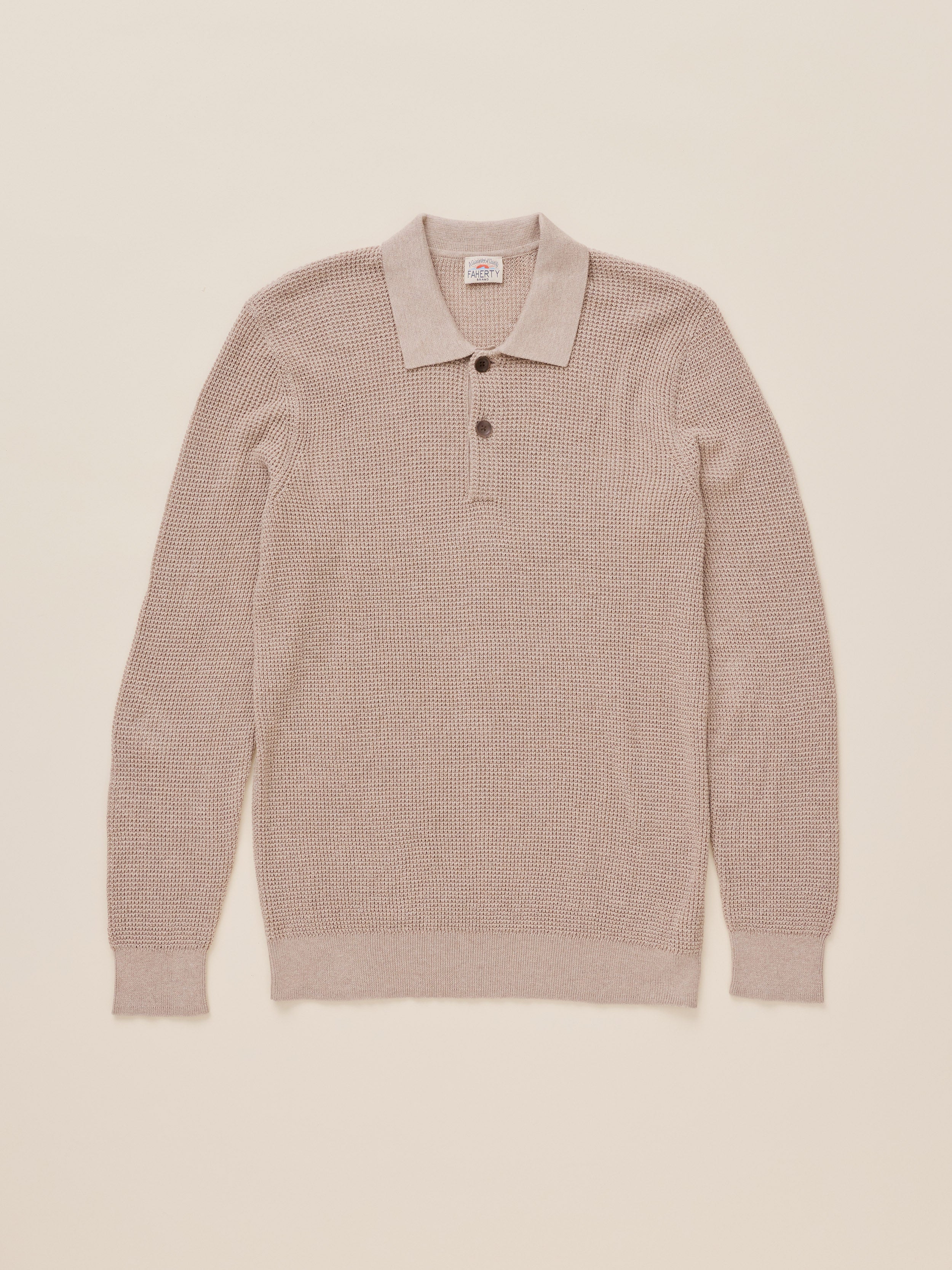 A light beige textured knit polo sweater with a collar and two-button placket, laid flat against a solid cream background.