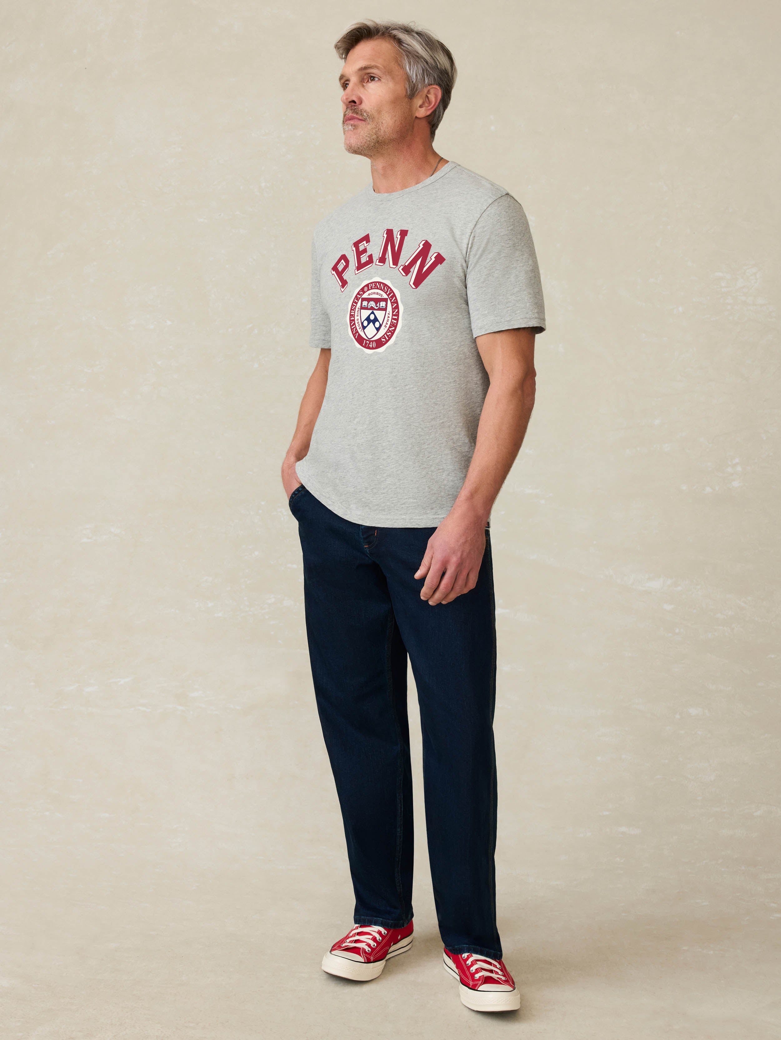 Man wearing a grey t-shirt with University of Pennsylvania graphic at the front against a beige background