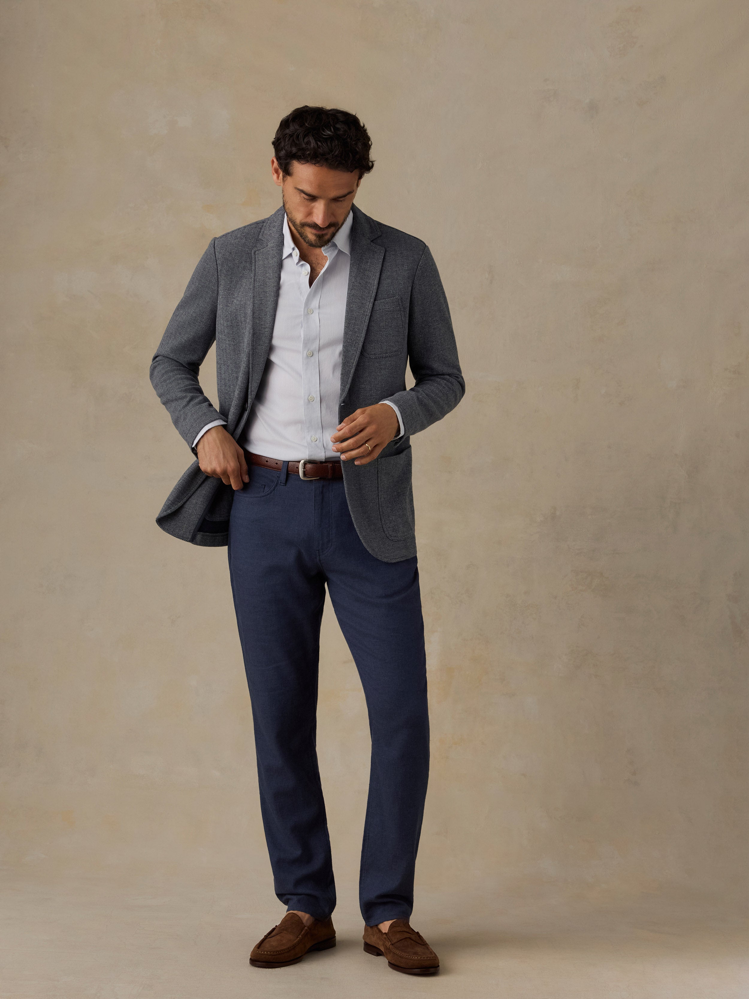 Man wearing a grey blazer and navy pants against a beige background
