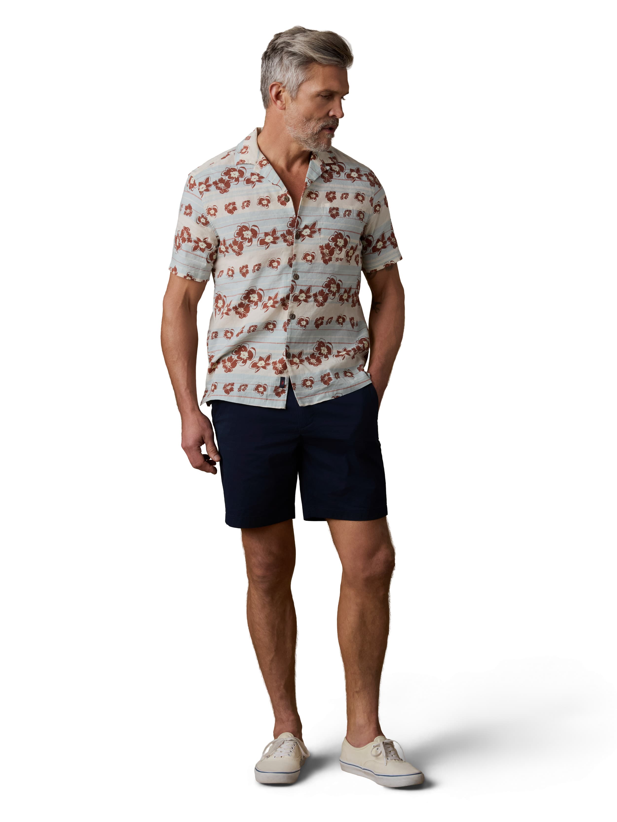 A man wearing a printed button up shirt, navy shorts, and white sneakers