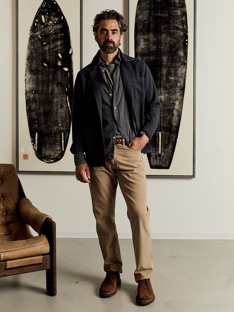 Model wearing stretch terry pants styled with a button up shirt, a chore coat and suede desert boots