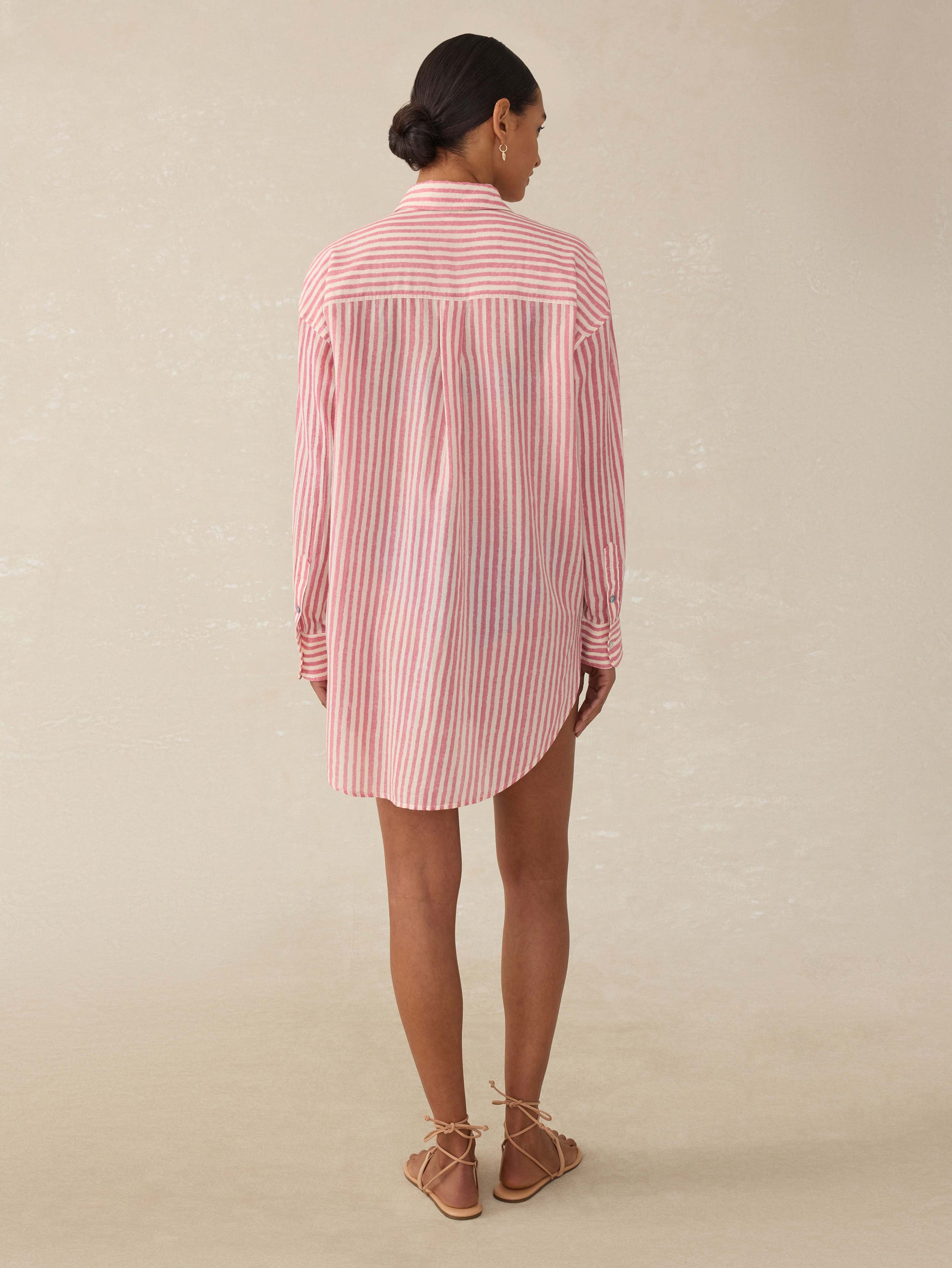 Back view of a woman wearing a pink and white striped shirt dress with Arizona State University graphic on the left chest against a beige background