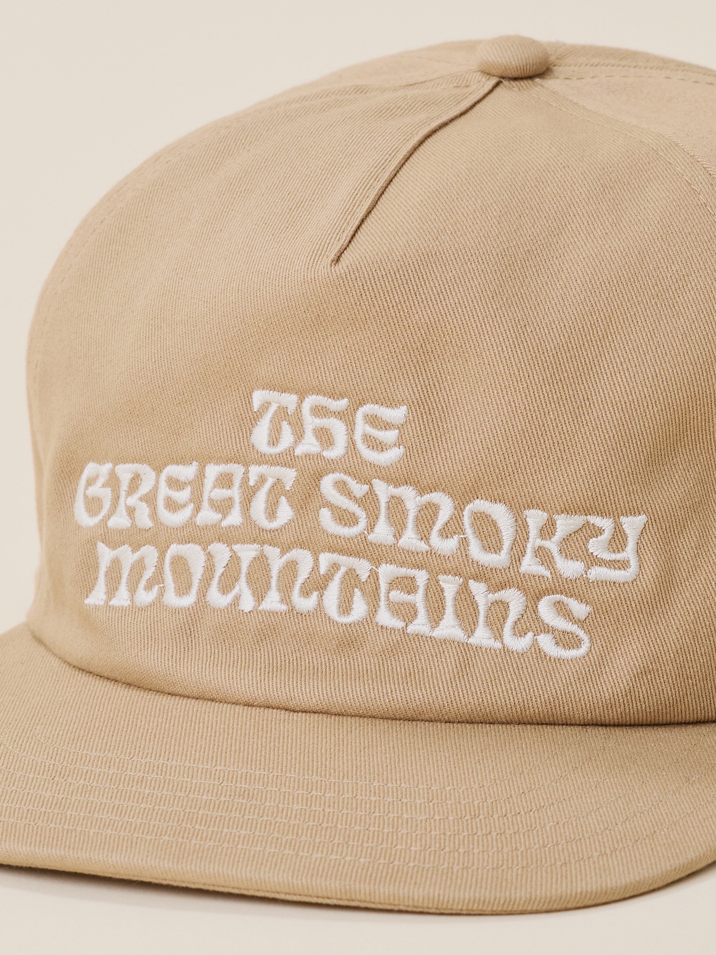 A close-up of a beige baseball cap with white embroidered text reading 'THE GREAT SMOKY MOUNTAINS' on the front panel.