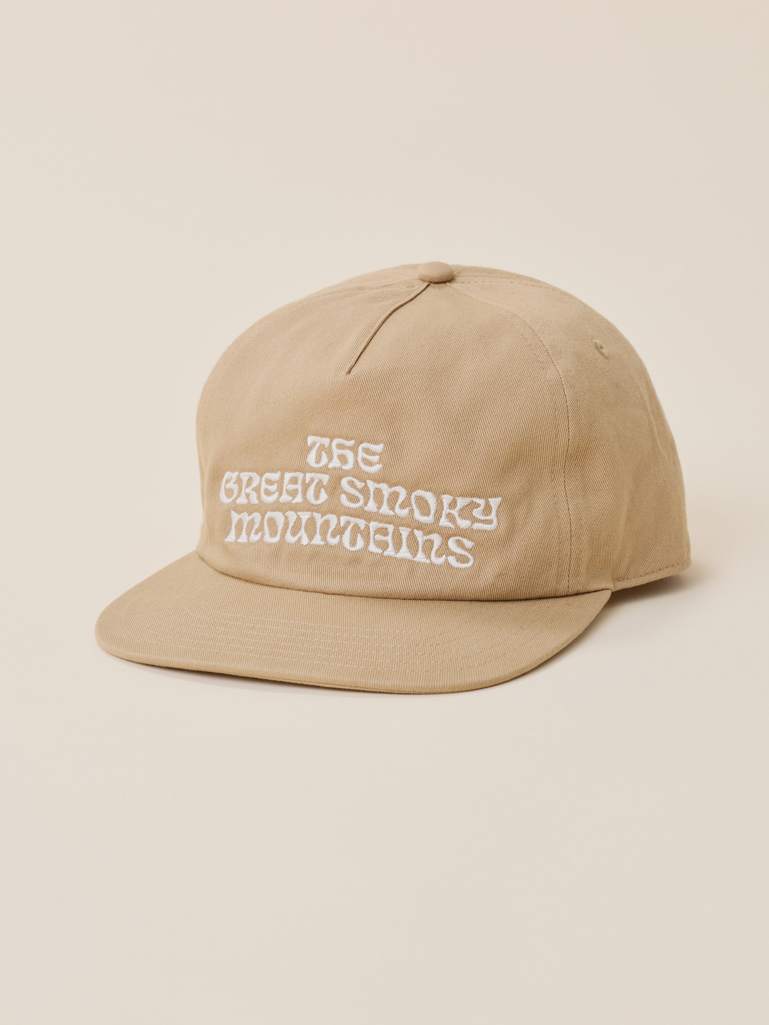 A beige baseball cap with white embroidered text reading 'THE GREAT SMOKY MOUNTAINS' on the front, photographed against a solid light beige background.