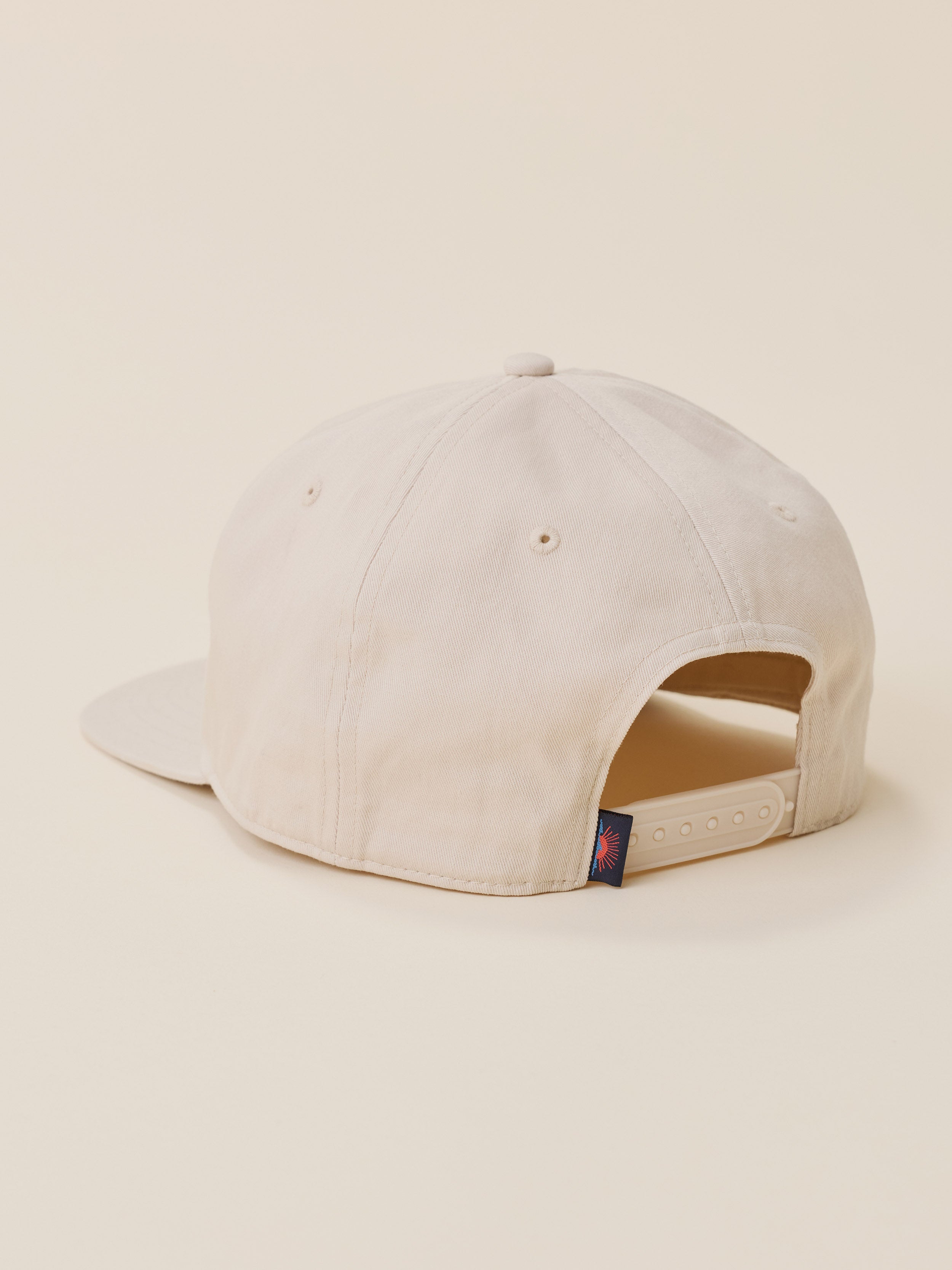 A light beige flat-brim baseball cap shown from a rear three-quarter angle against a solid cream background.