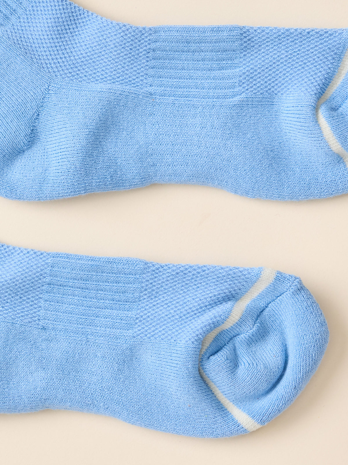 A pair of light blue knit crew socks with white contrast stitching, laid flat on a warm beige background., image 3 of 3