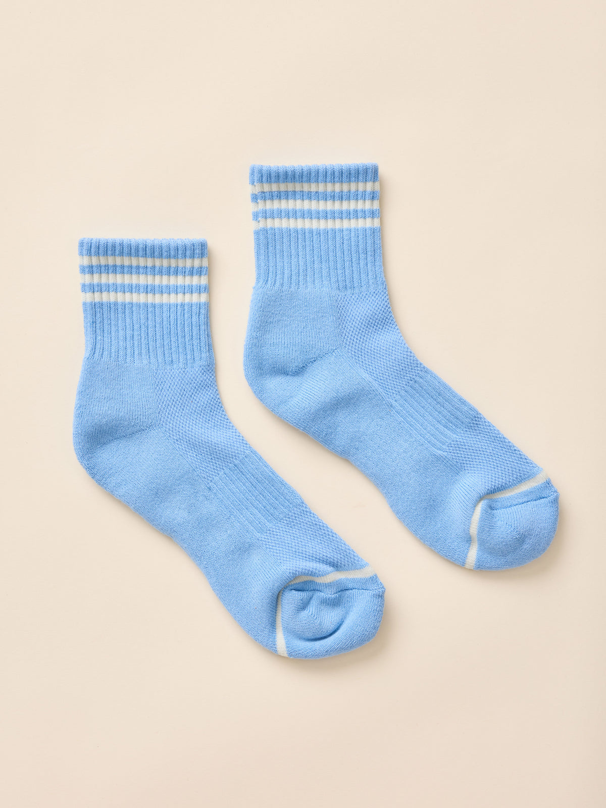 A pair of light blue knit crew socks with white contrast stitching, laid flat on a warm beige background., image 2 of 3
