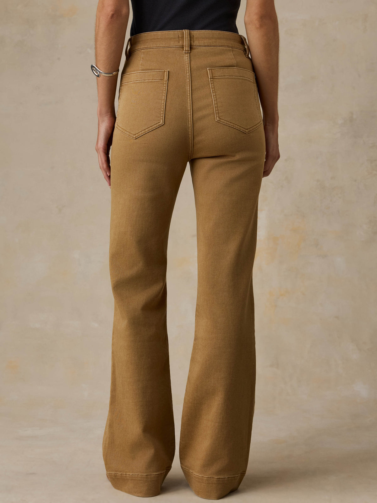 Woman wearing a black tank top and brown pants against a beige background, image 3 of 6