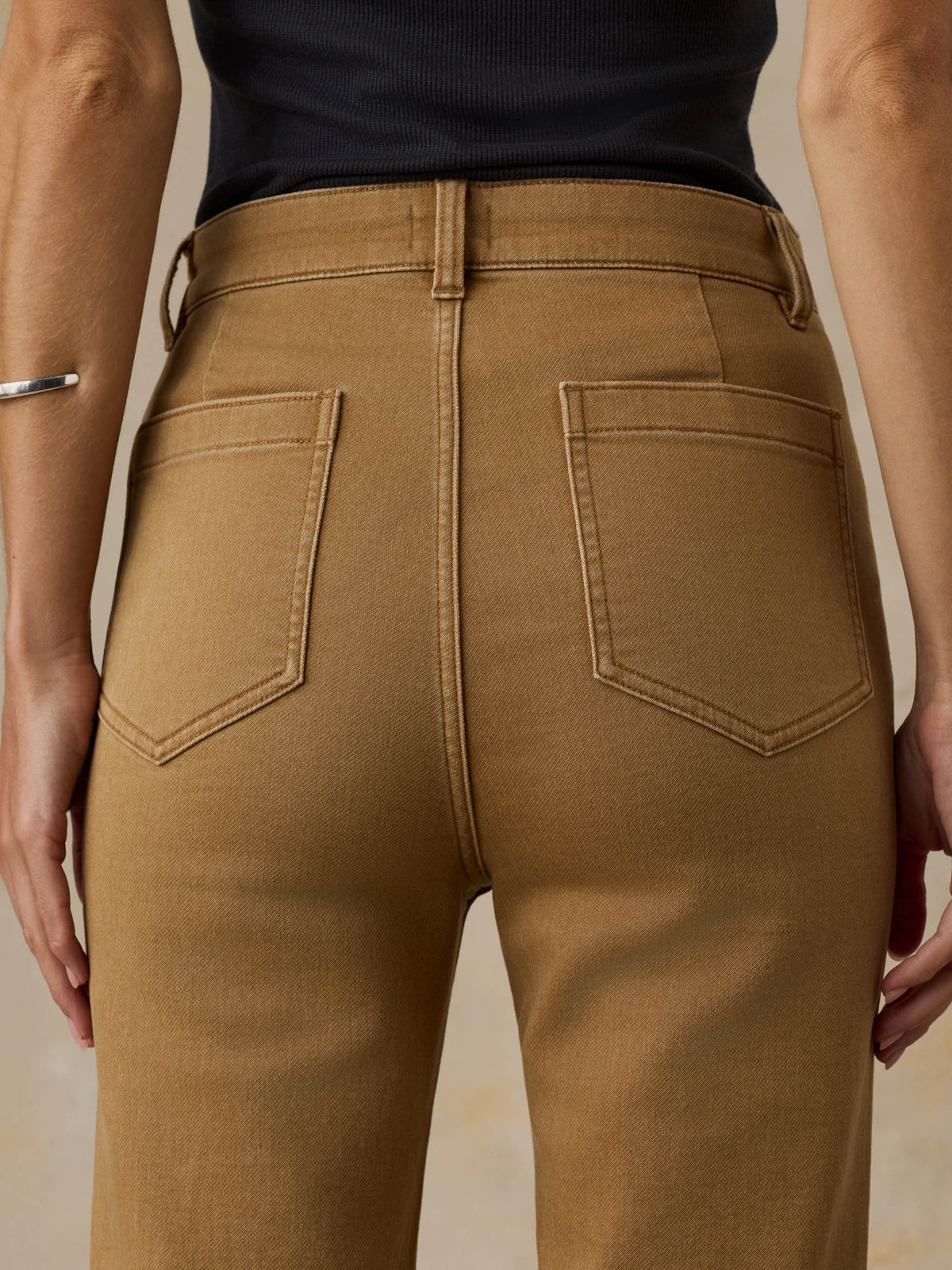 Woman wearing a black tank top and brown pants against a beige background, image 6 of 6