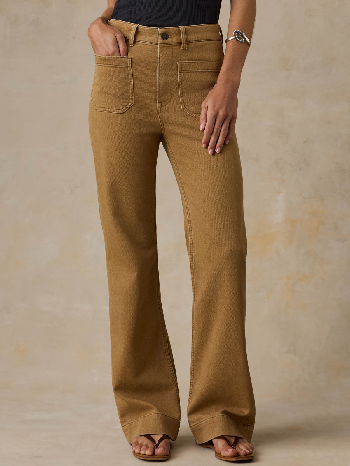 Woman wearing a black tank top and brown pants against a beige background, image 2 of 6
