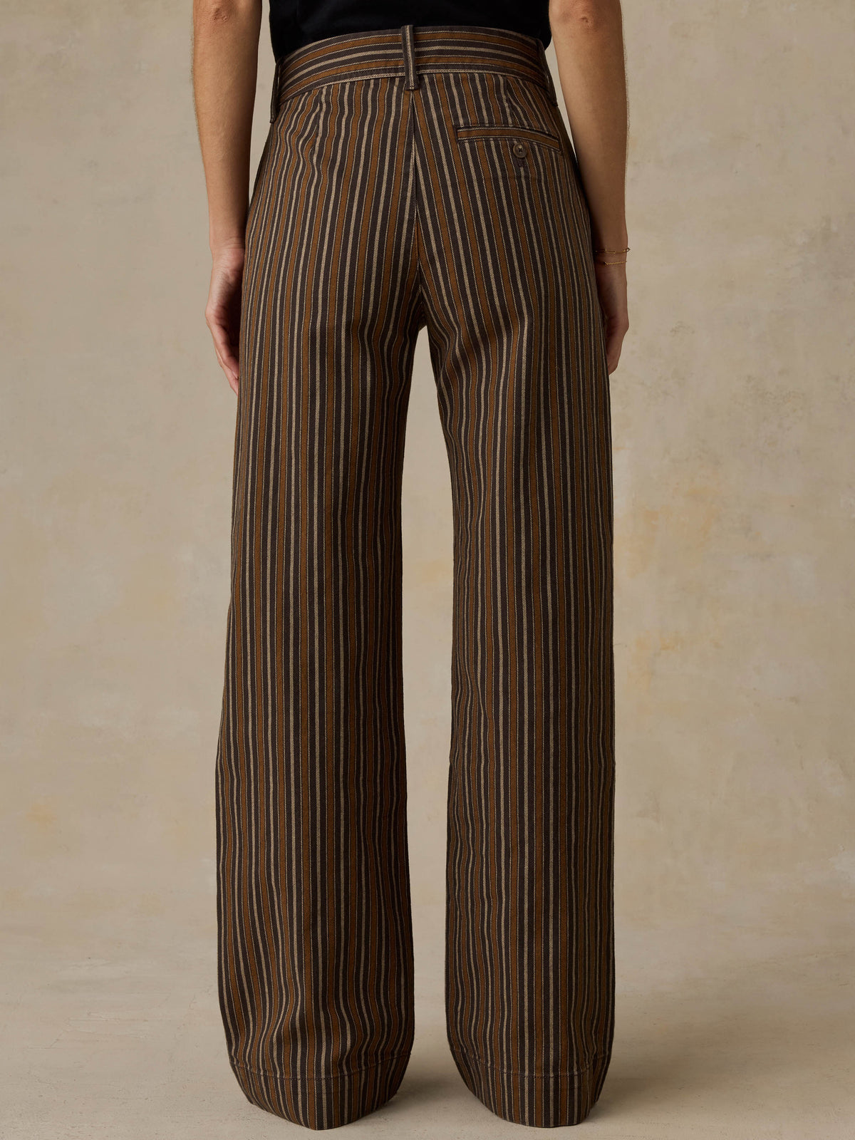Woman wearing a black t-shirt and brown striped pants on a beige background, image 3 of 7