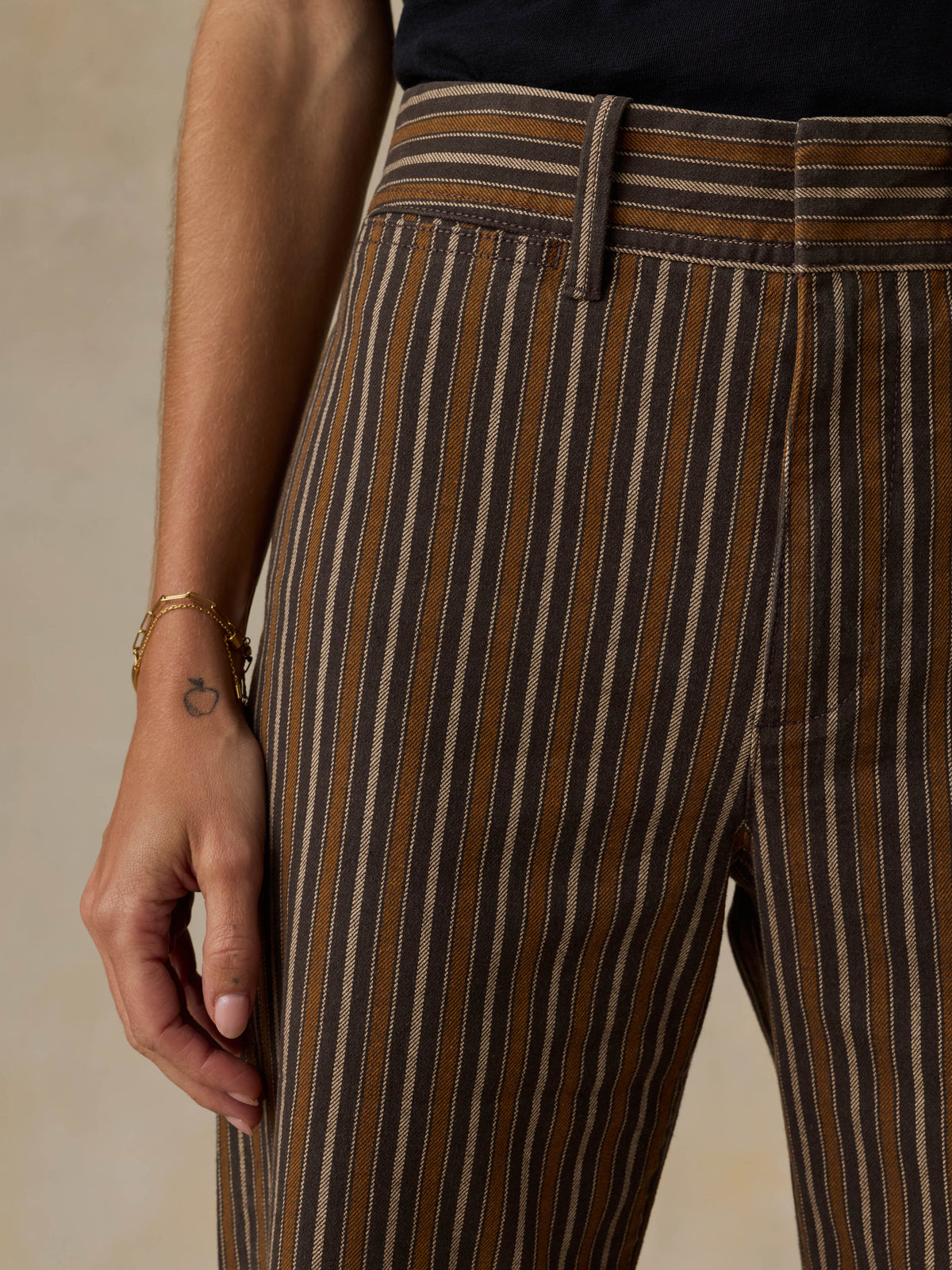 Woman wearing a black t-shirt and brown striped pants on a beige background, image 5 of 7