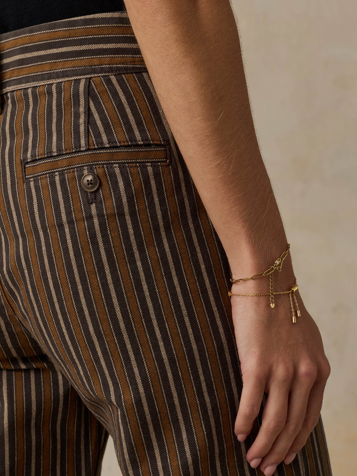 Woman wearing a black t-shirt and brown striped pants on a beige background, image 6 of 7