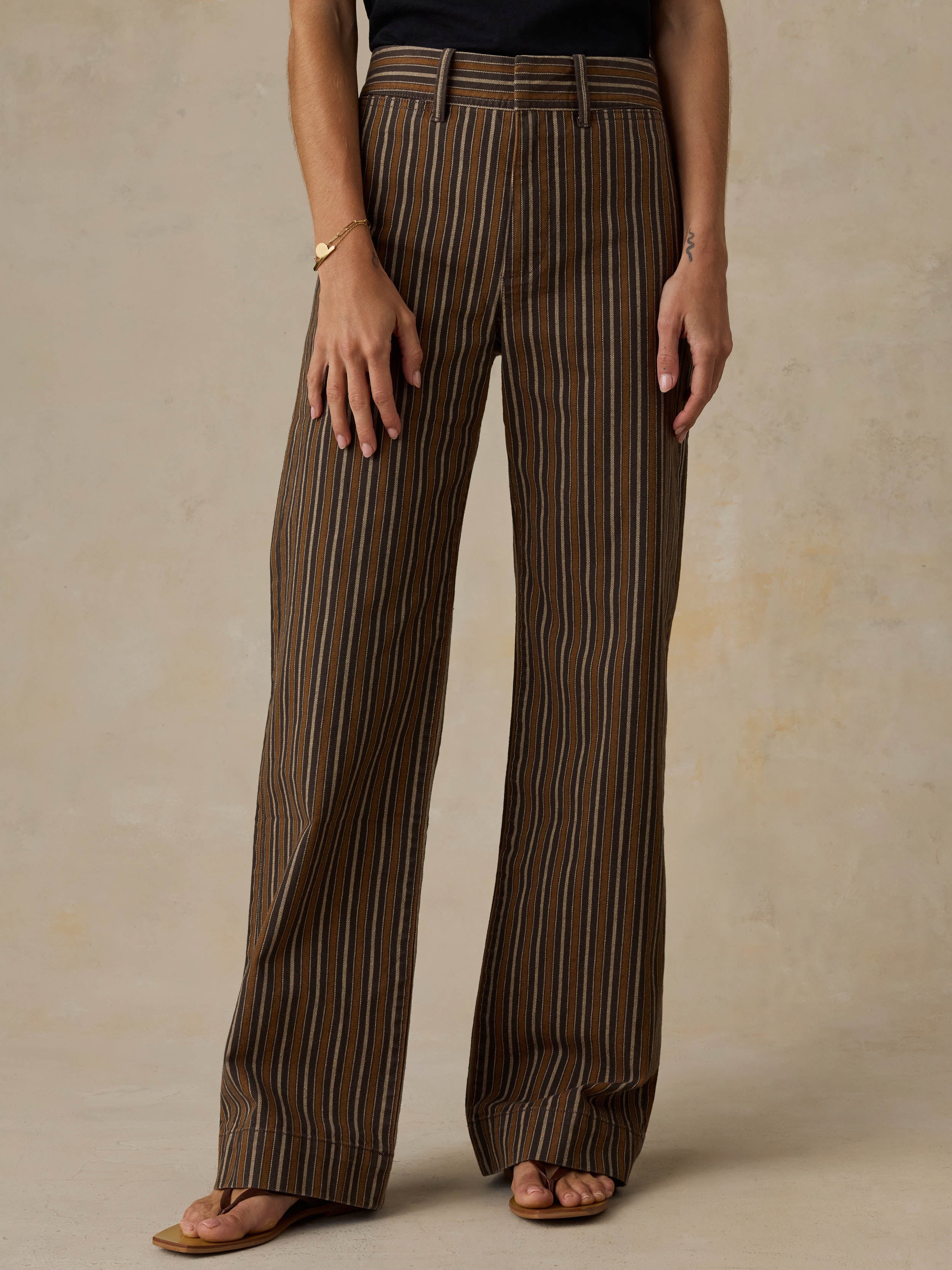 Woman wearing a black t-shirt and brown striped pants on a beige background