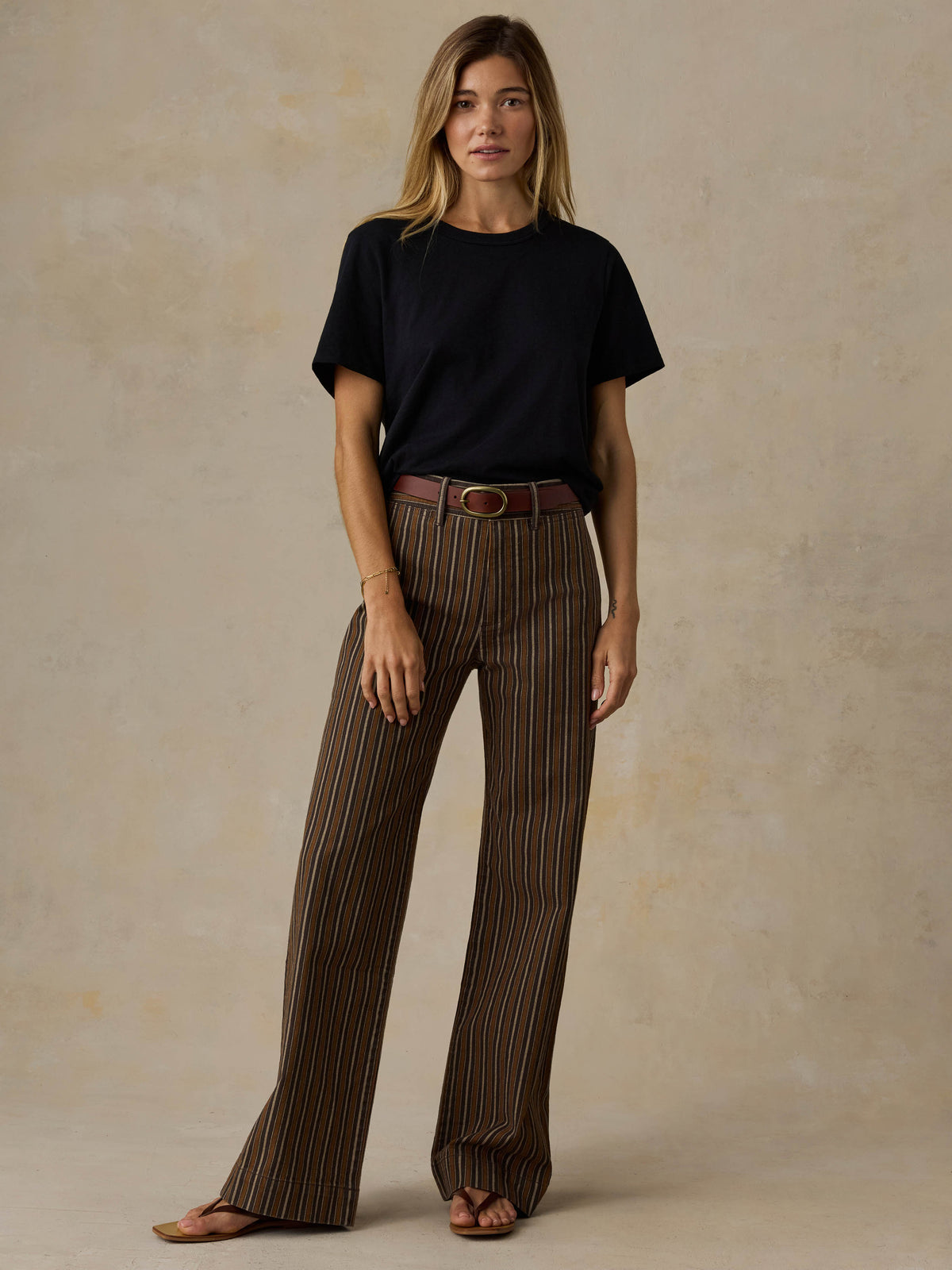 Woman wearing a black t-shirt and brown striped pants on a beige background, image 2 of 7