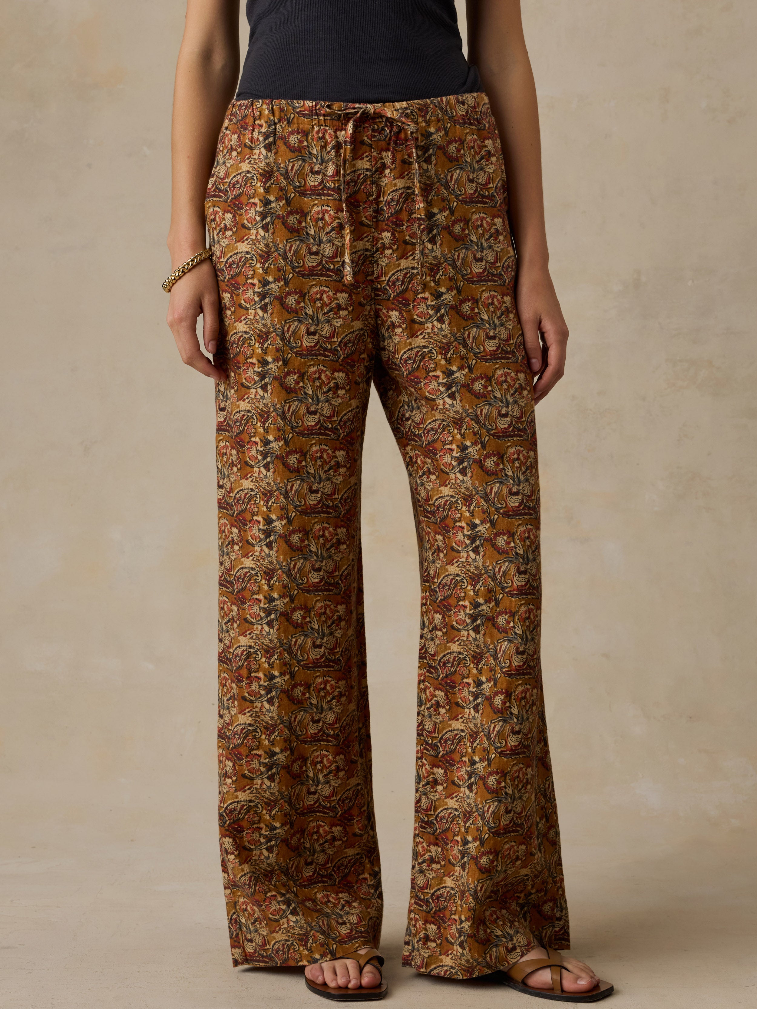 Woman wearing a black top with orange floral printed pants against a beige background