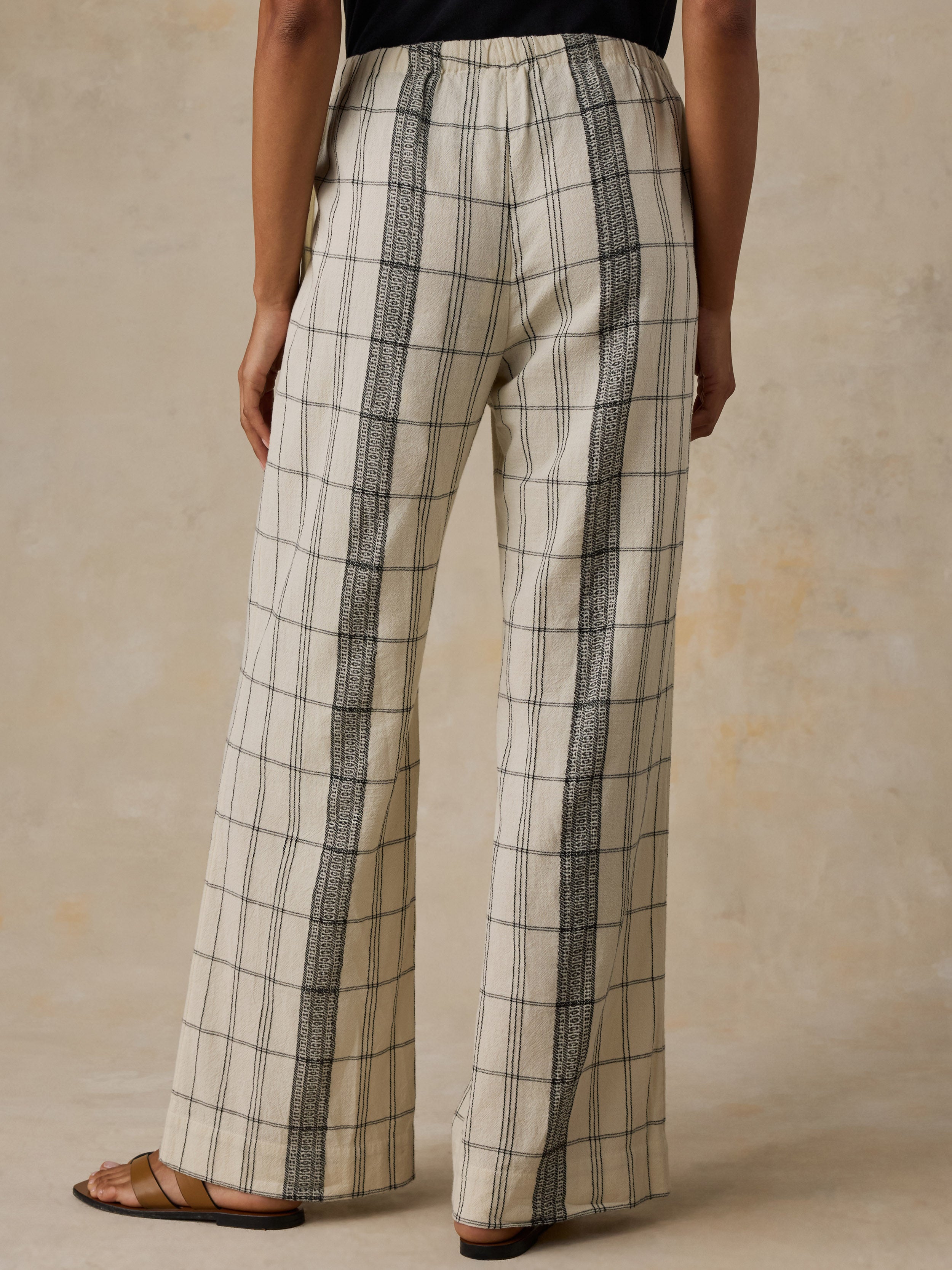 Woman wearing a black t-shirt and white and black plaid pants against a beige background
