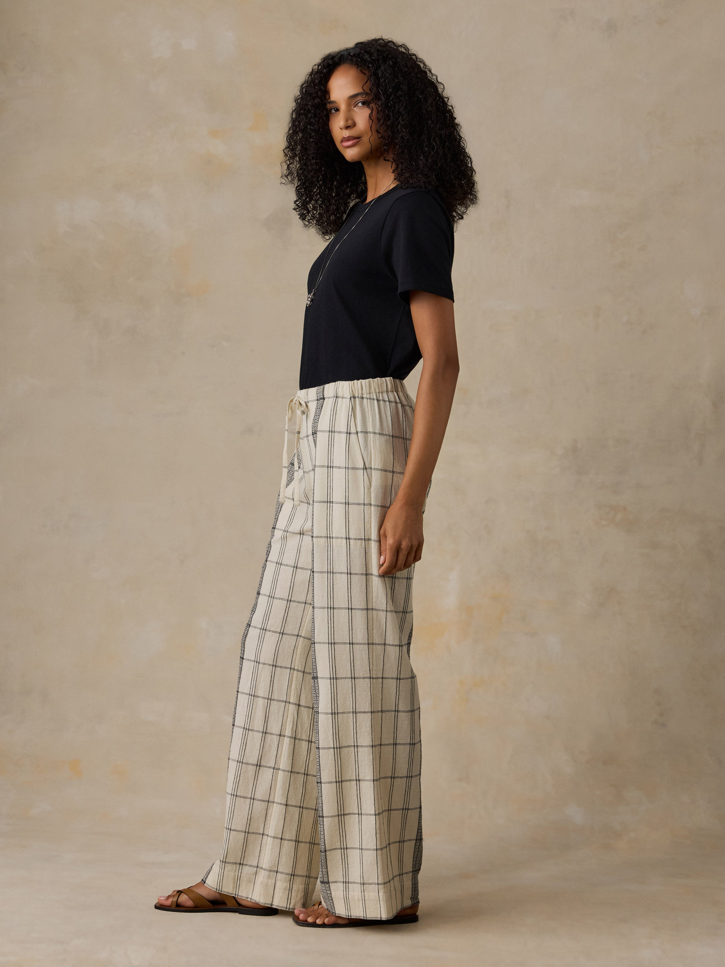Woman wearing a black t-shirt and white and black plaid pants against a beige background
