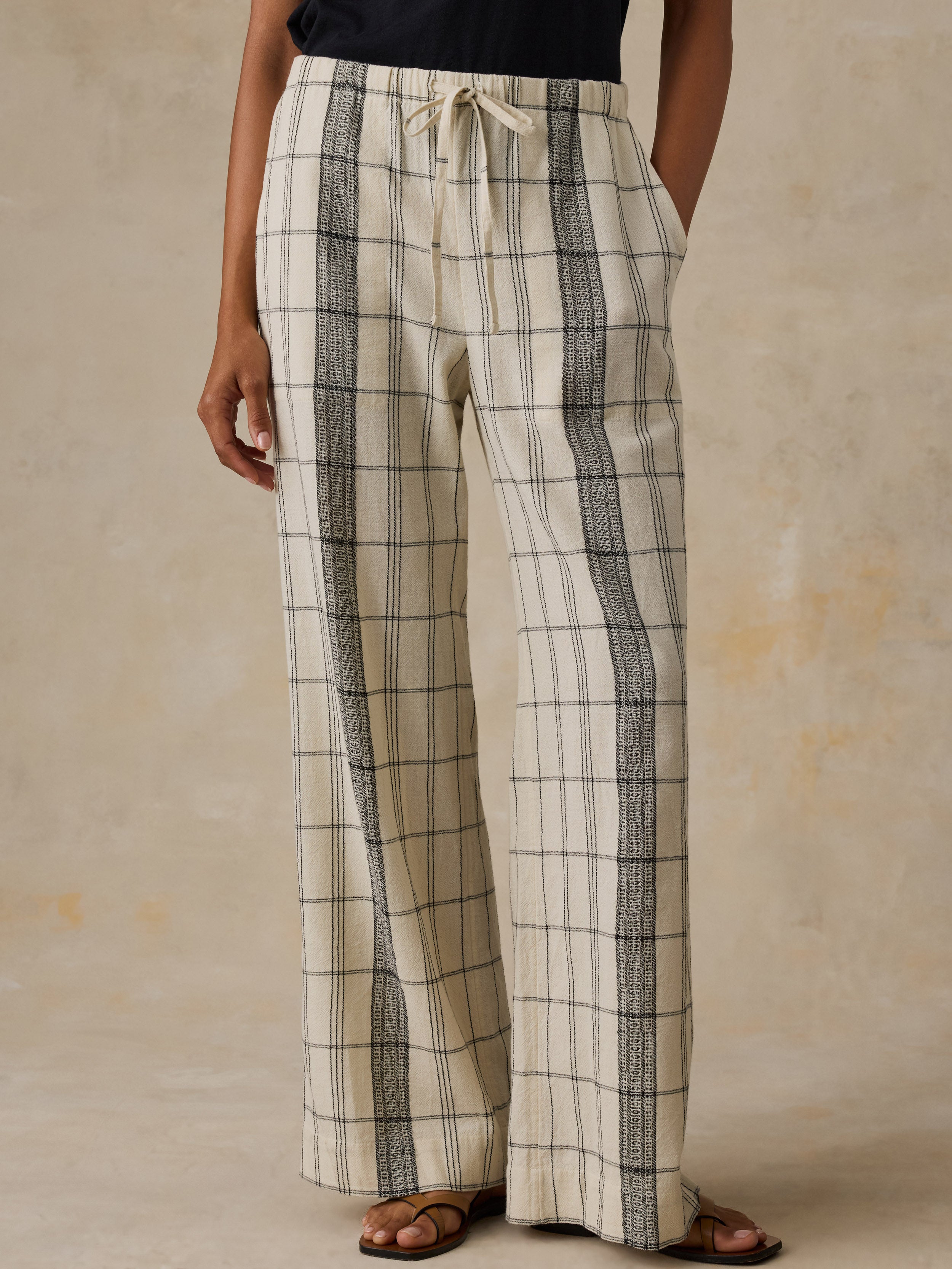 Woman wearing a black t-shirt and white and black plaid pants against a beige background