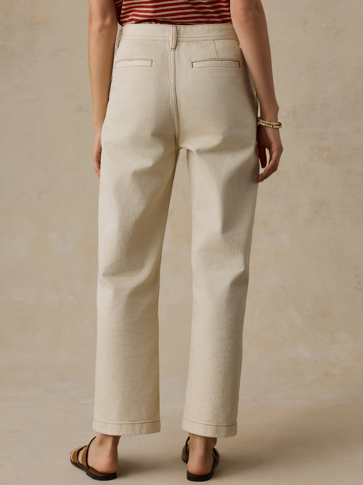 Woman wearing a red and white striped t-shirt and cream colored denim jeans against a beige background, image 5 of 7