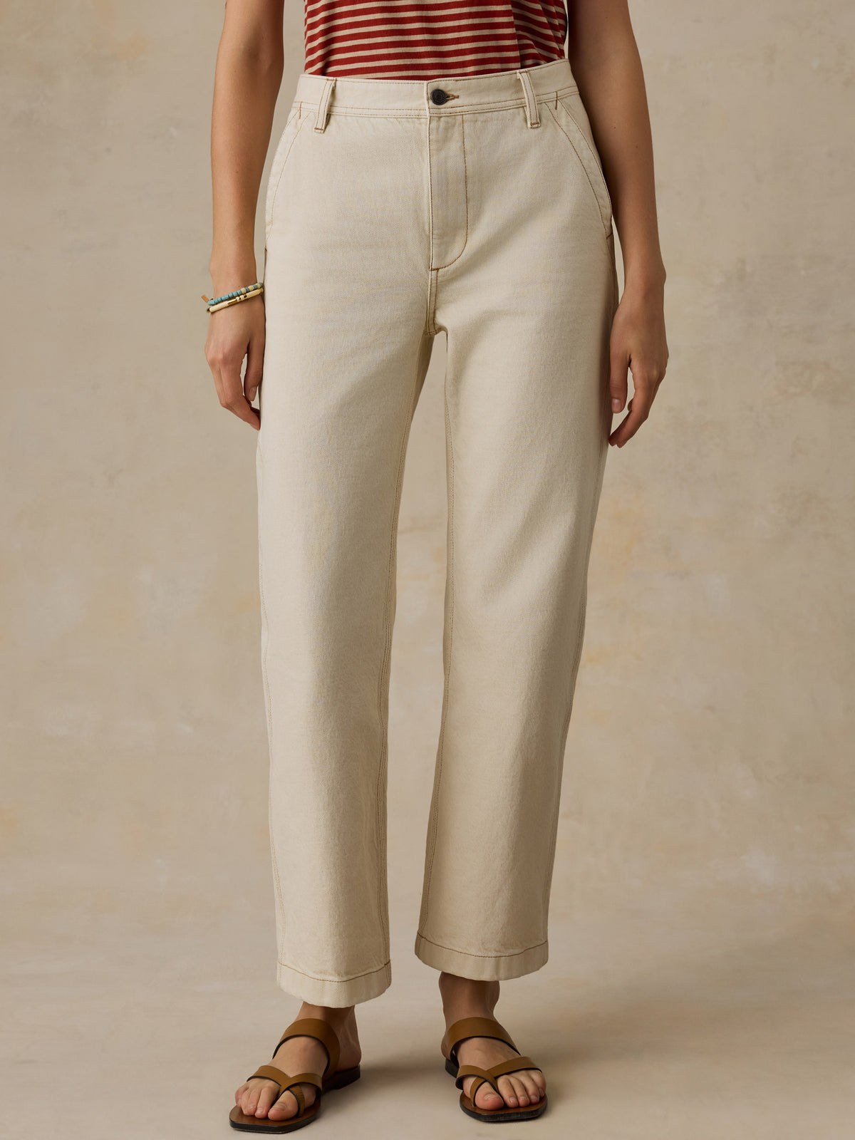 Woman wearing a red and white striped t-shirt and cream colored denim jeans against a beige background, image 2 of 7