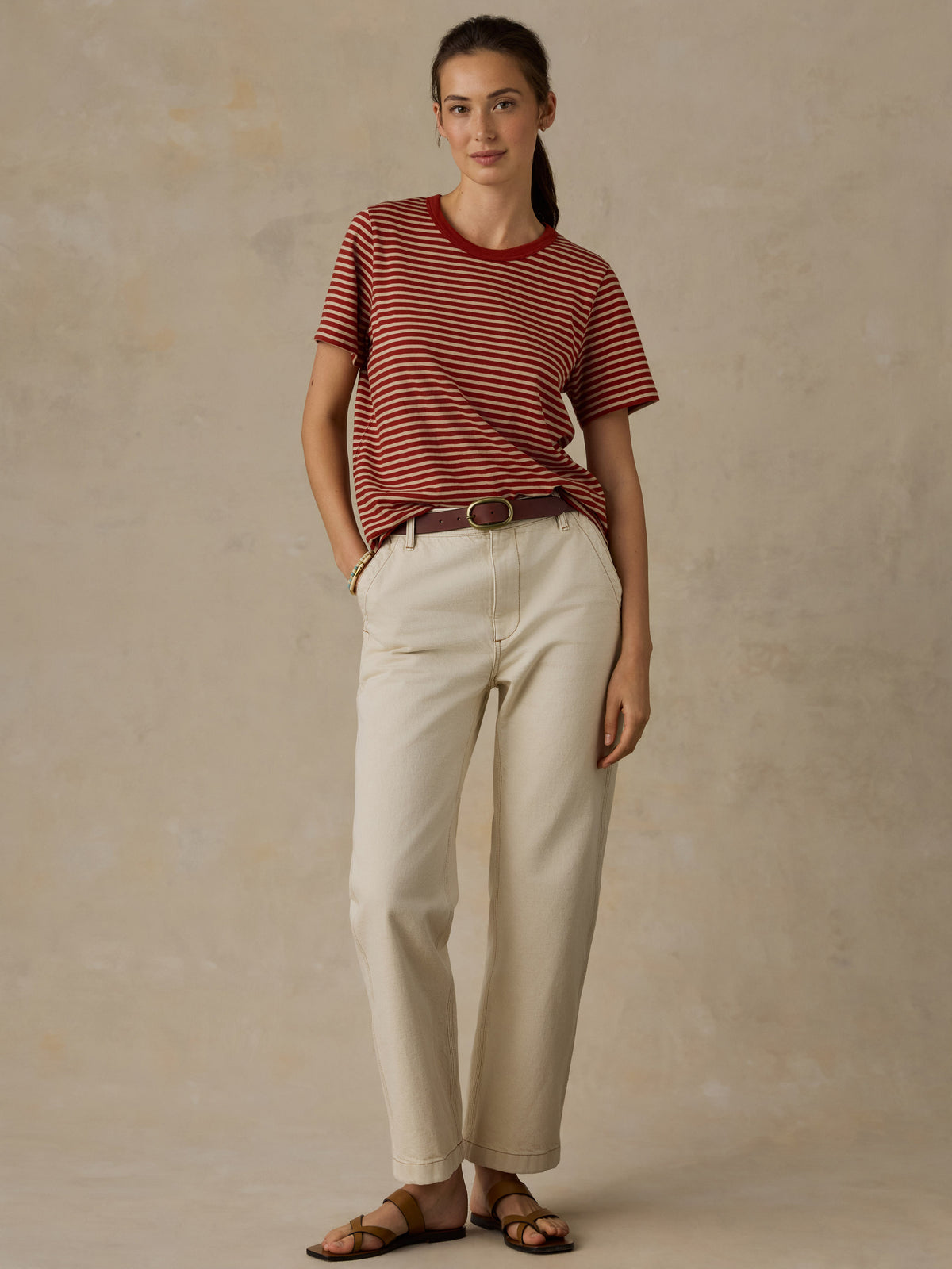 Woman wearing a red and white striped t-shirt and cream colored denim jeans against a beige background, image 3 of 7