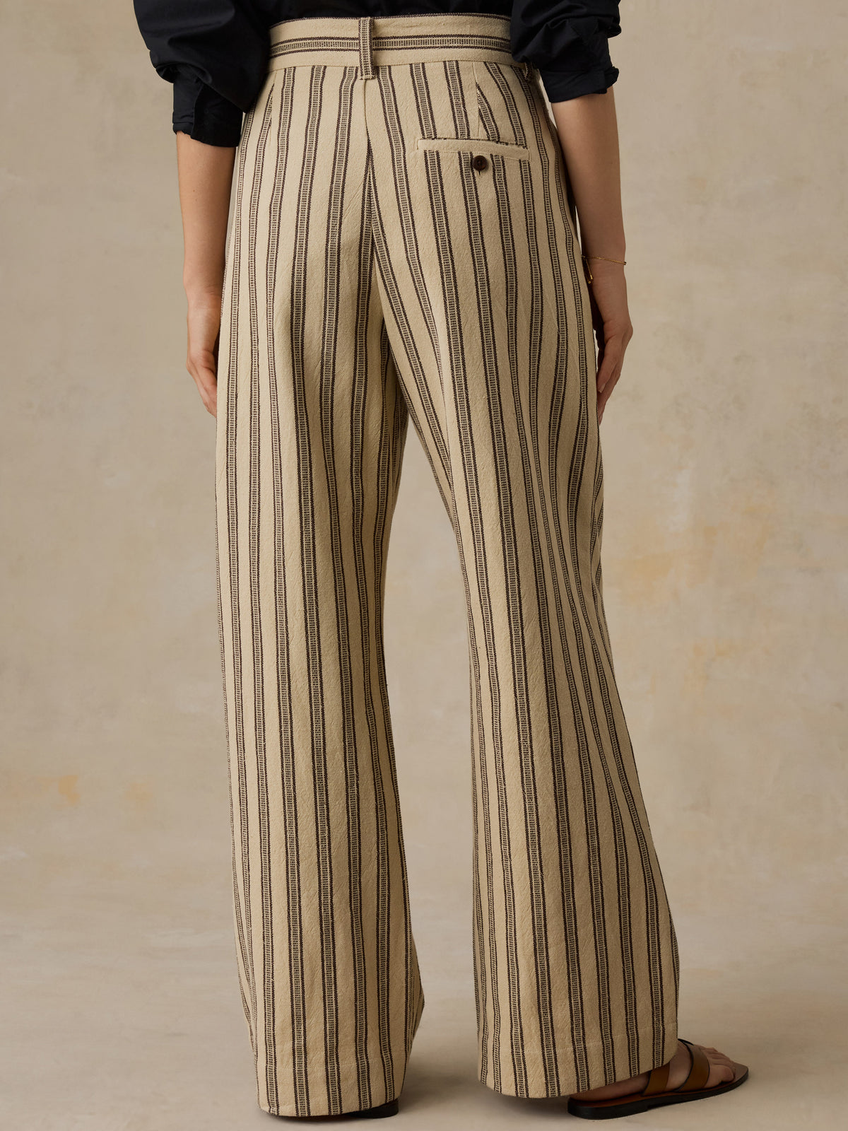 Woman wearing a black button down shirt and beige and black striped pants against a beige background. , image 4 of 6