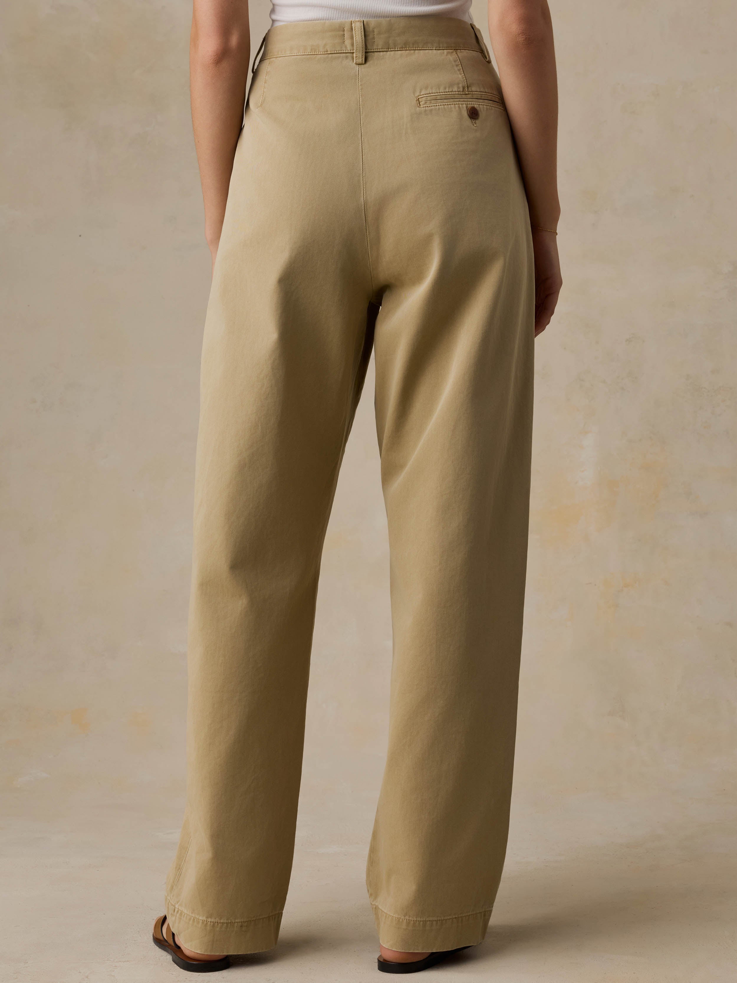 Woman wearing a white tank top and beige pants against a beige background