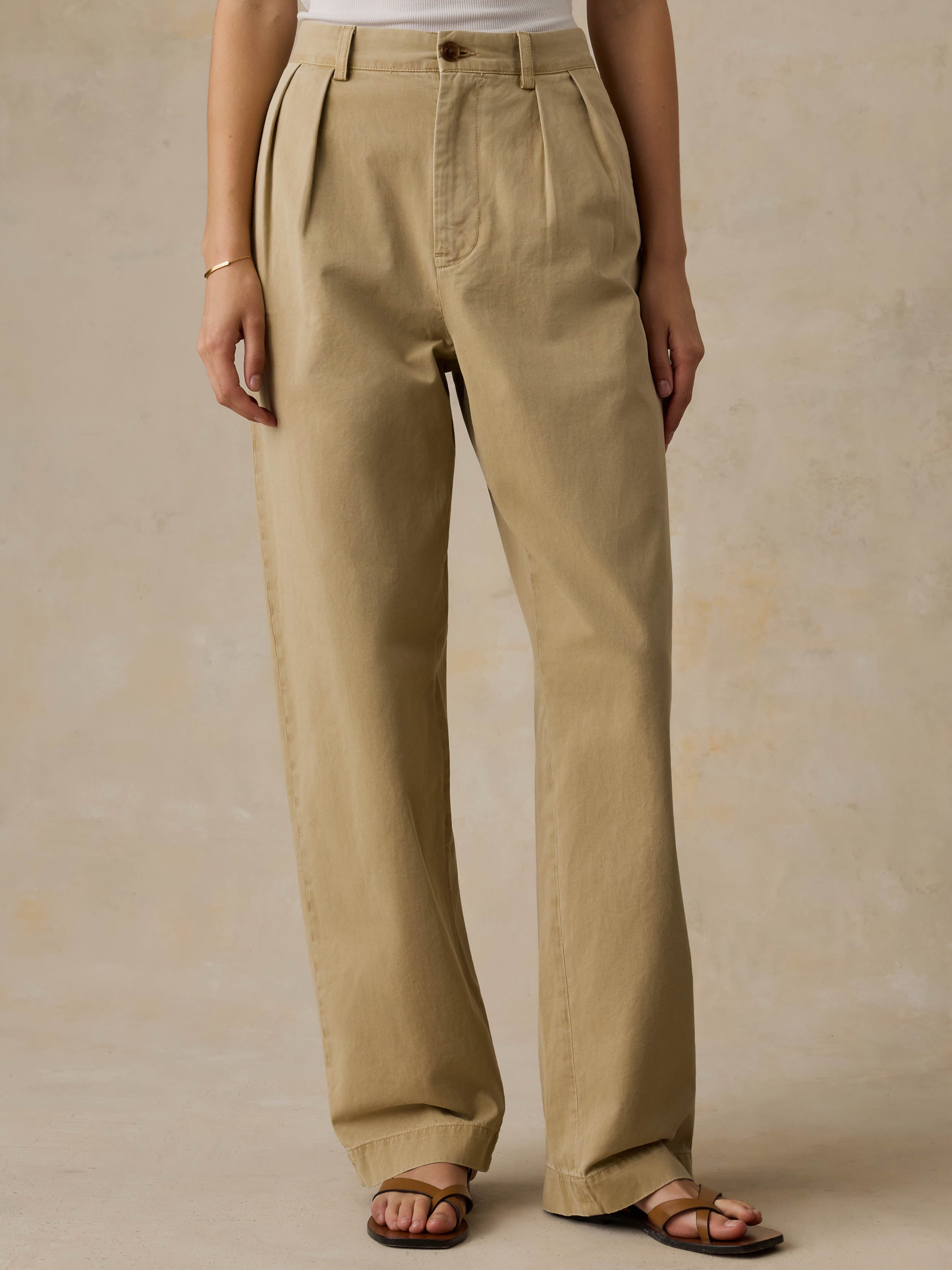 Woman wearing a white tank top and beige pants against a beige background
